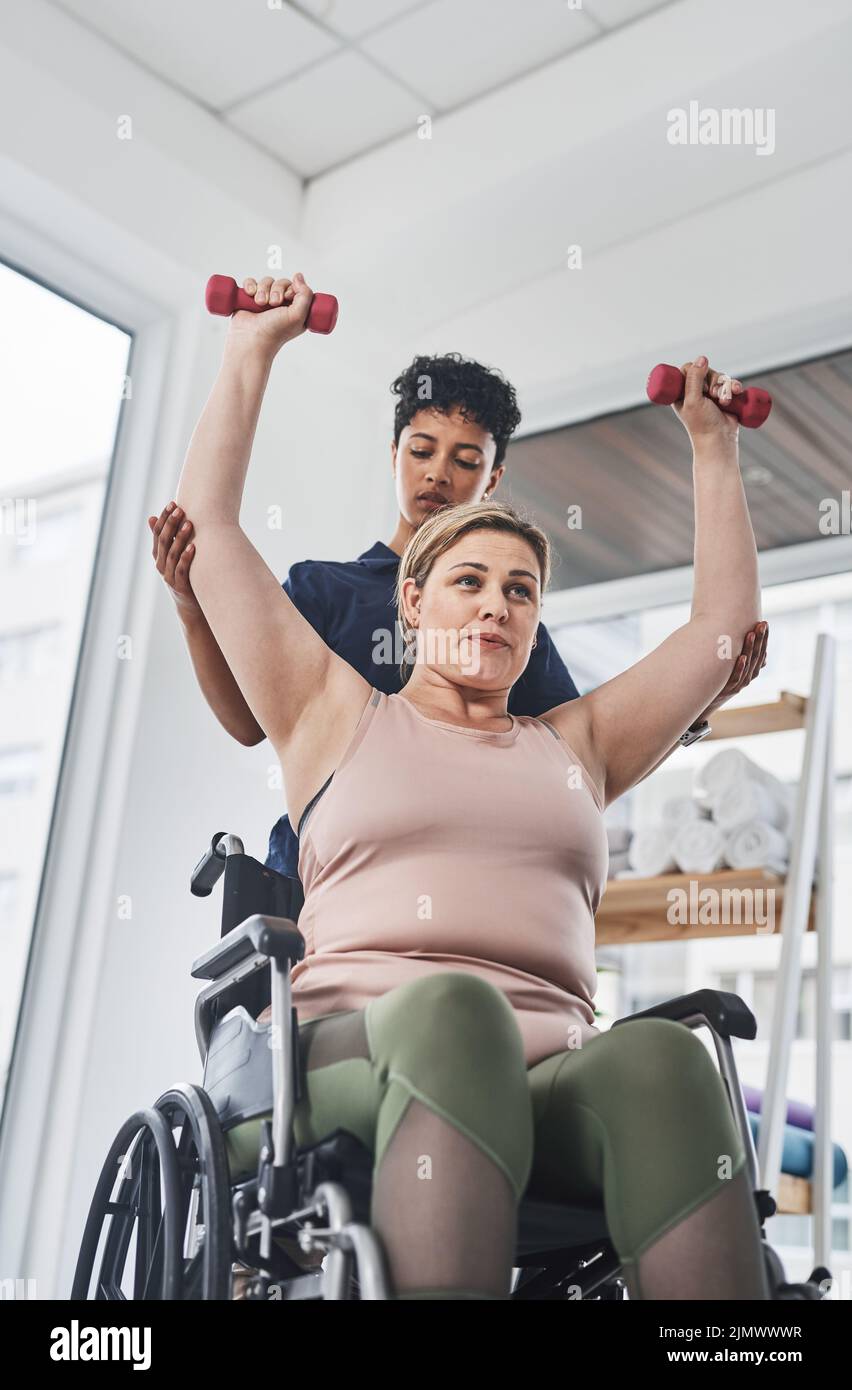 Ne laissez pas une blessure vous peser vers le bas. Un jeune physiothérapeute qui aide son patient en fauteuil roulant à faire de l'exercice avec des haltères dans une clinique. Banque D'Images