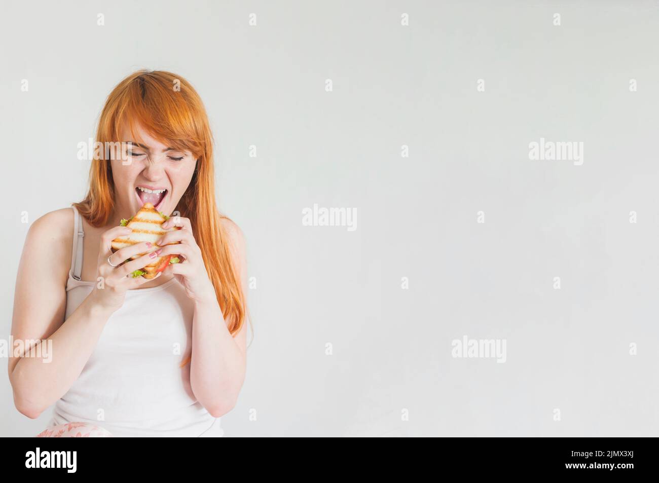 Une jeune femme affamée mange un sandwich grillé sur fond blanc Banque D'Images