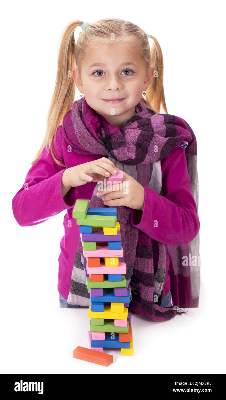 Les hobbies des enfants, la créativité, une petite fille dans une robe bleue jouant avec le jeu de bois jenga sur fond blanc Banque D'Images