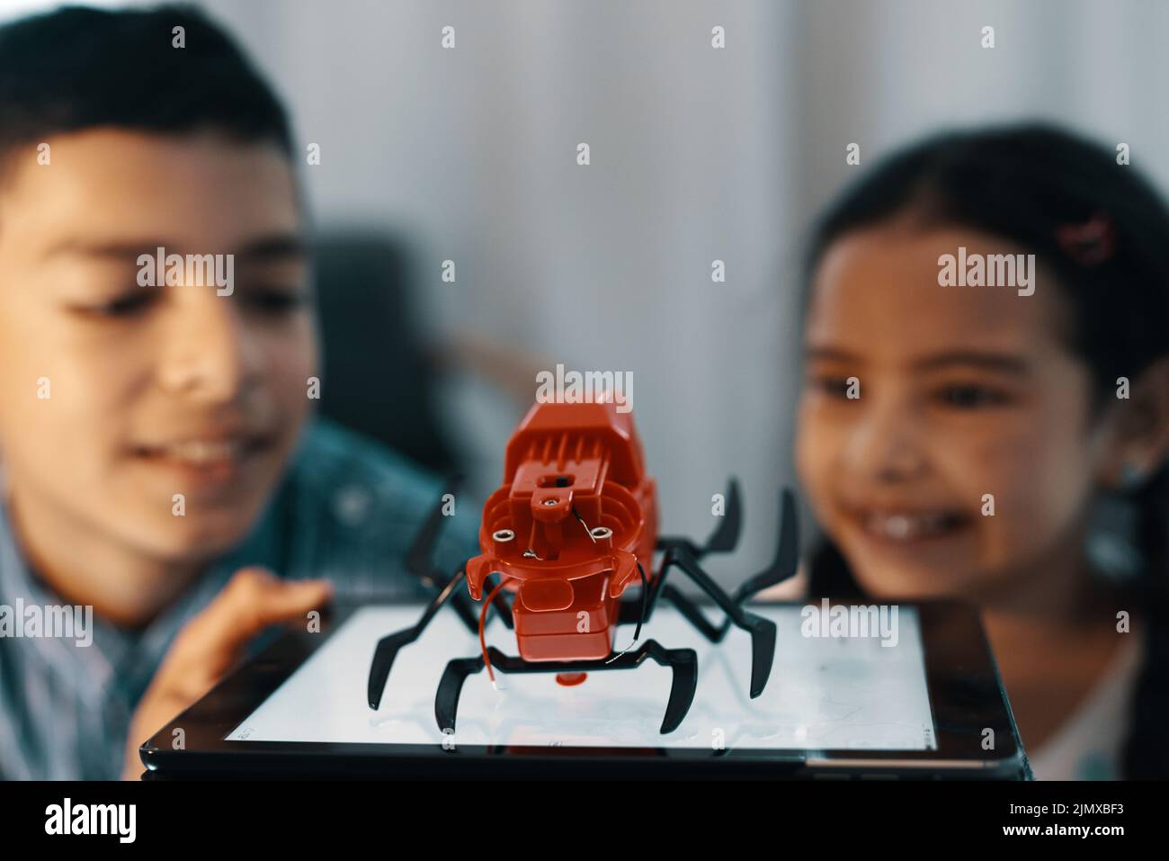 Nous nous sommes surfaits sur celui-ci. Deux jeunes frères et sœurs regardent et admirent leur araignée de jouet robotique à la maison. Banque D'Images
