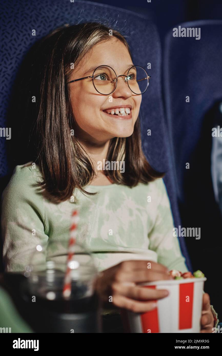 Portrait vertical moyen d'une fille qui s'amuse à regarder un film de comédie et à manger du pop-corn au cinéma Banque D'Images