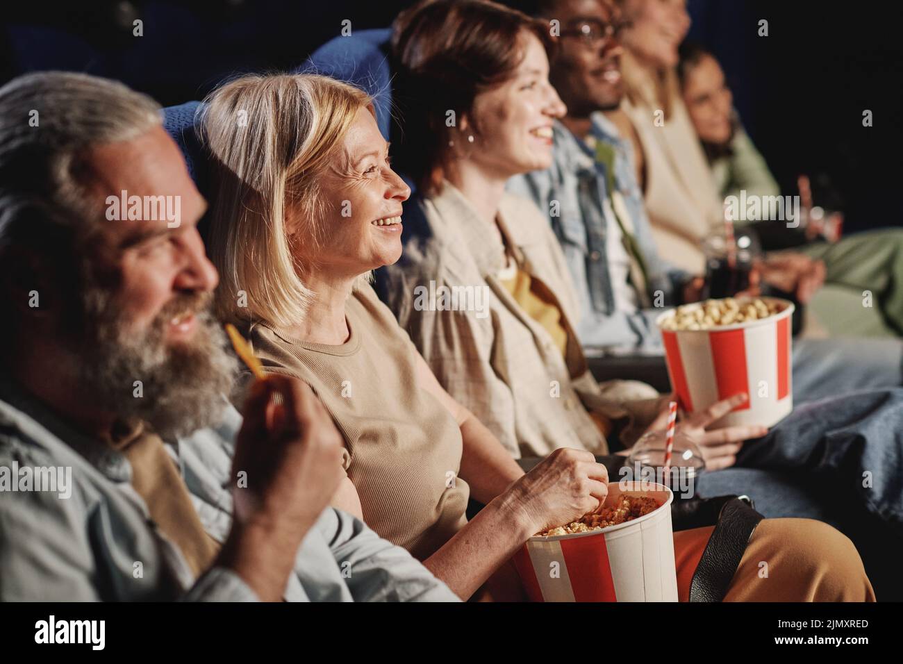 Grand angle de groupe de personnes diverses appréciant regarder des films de comédie et de prendre des collations au cinéma Banque D'Images