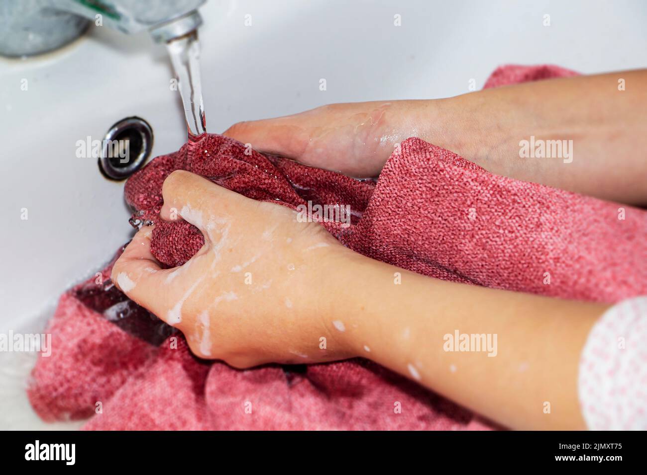 Lavage à la main des articles de couleur. Les mains des femmes se lavent et essorent les articles de couleur dans de l'eau savonneuse Banque D'Images