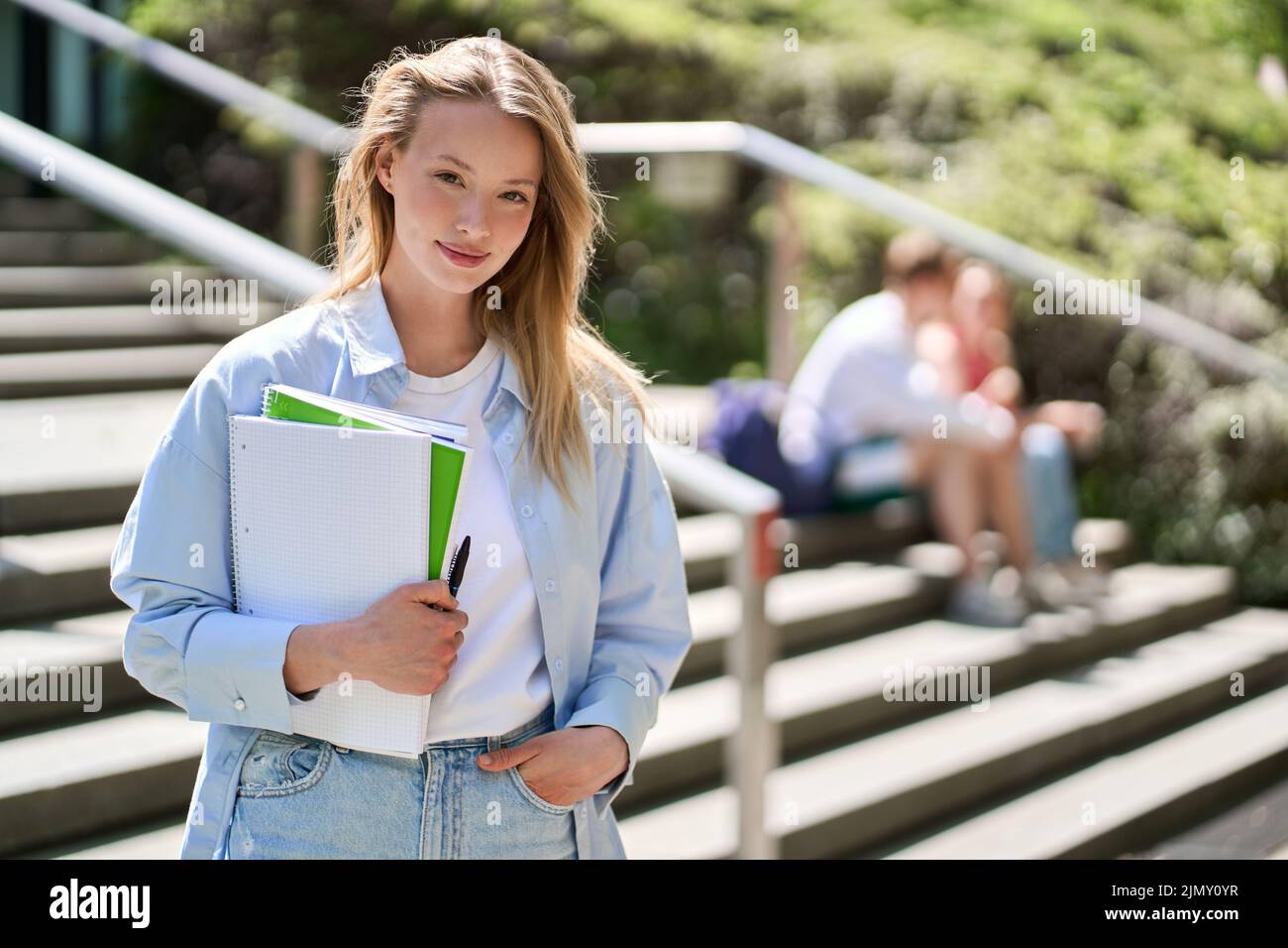 Jolie jeune fille étudiante à l'université tenant des cahiers posant pour un portrait en plein air. Banque D'Images