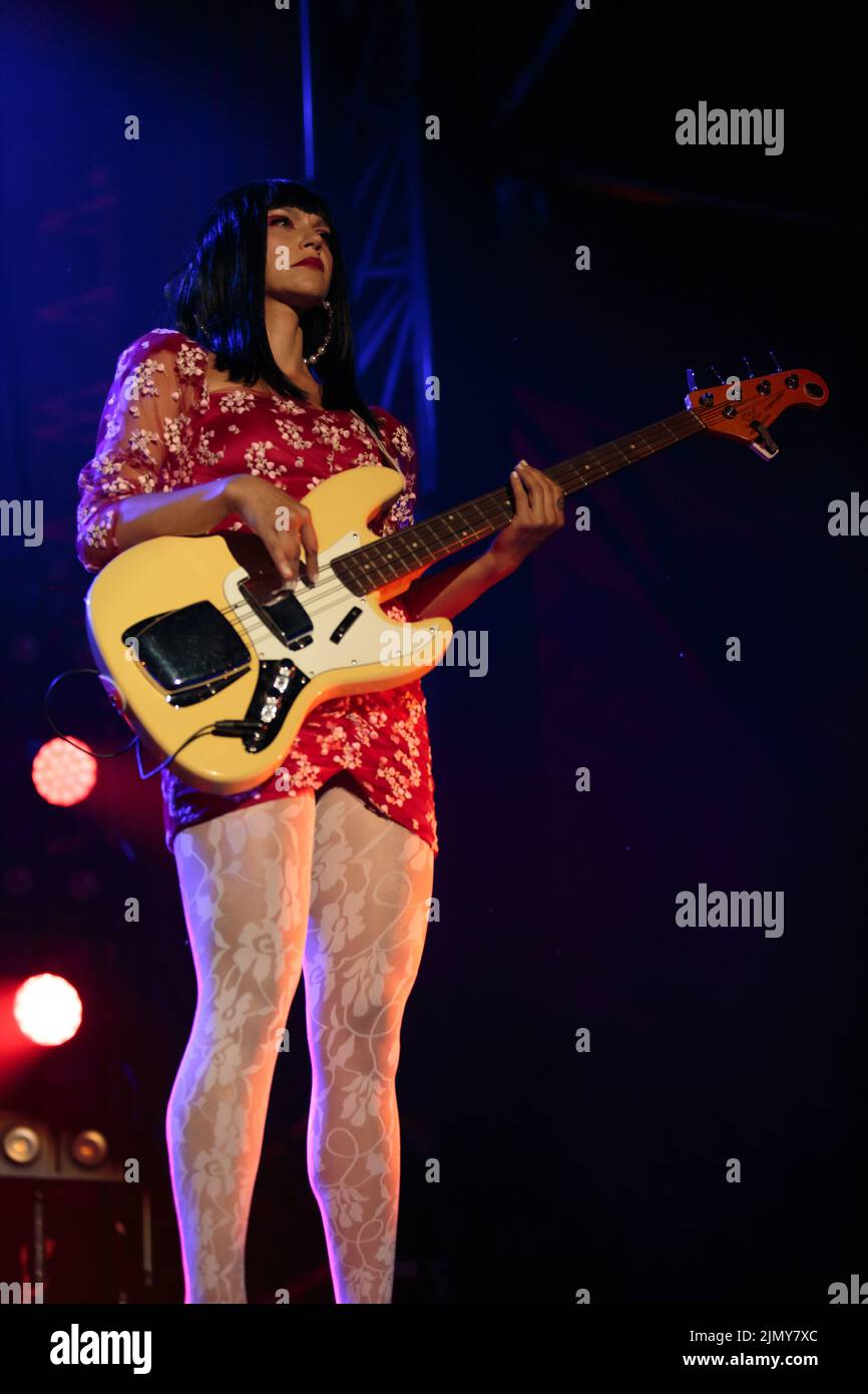 Bassiste Laura Lee de Khruangbin sur scène portant une petite robe à motif floral rouge avec des bas blancs Banque D'Images