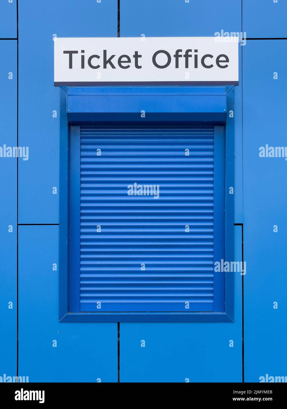 Fenêtre de la billetterie avec volet métallique tiré vers le bas, dans la façade extérieure d'un bâtiment contemporain aux murs bleus Banque D'Images