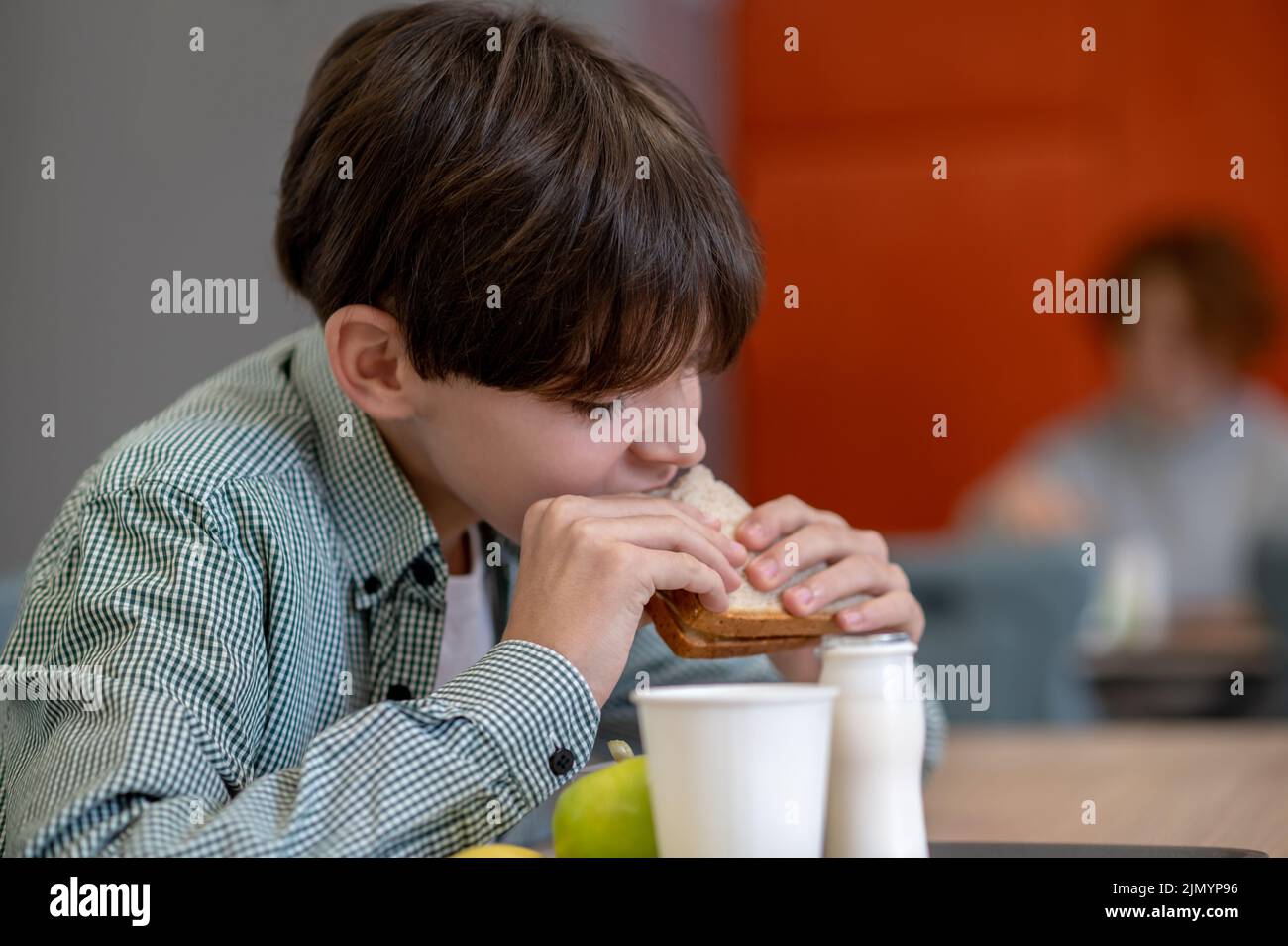 Un garçon aux cheveux foncés mangeant un sandwich dans une cantine scolaire Banque D'Images