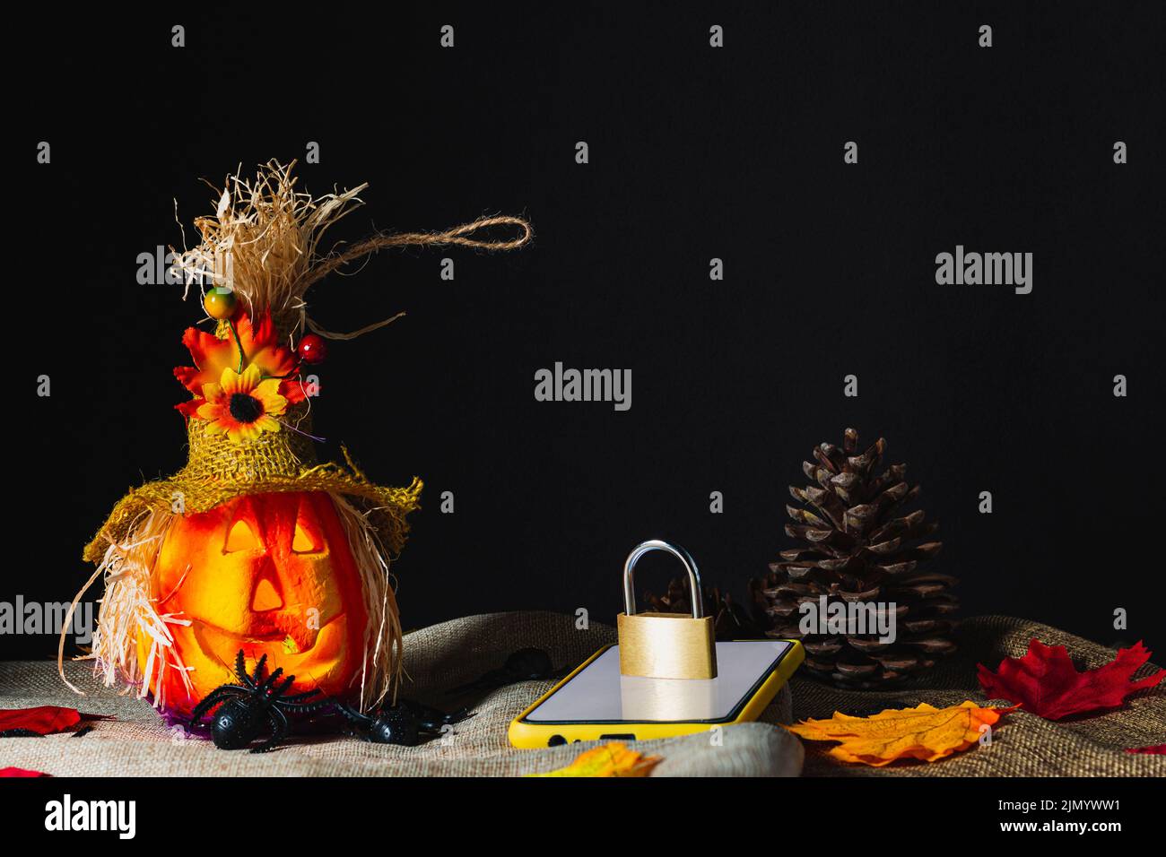Téléphone cellulaire avec un étui jaune, avec l'écran allumé et un cadenas verrouillé sur le dessus à côté d'une citrouille d'Halloween ornée de tissu de sac et entouré de jouets Banque D'Images