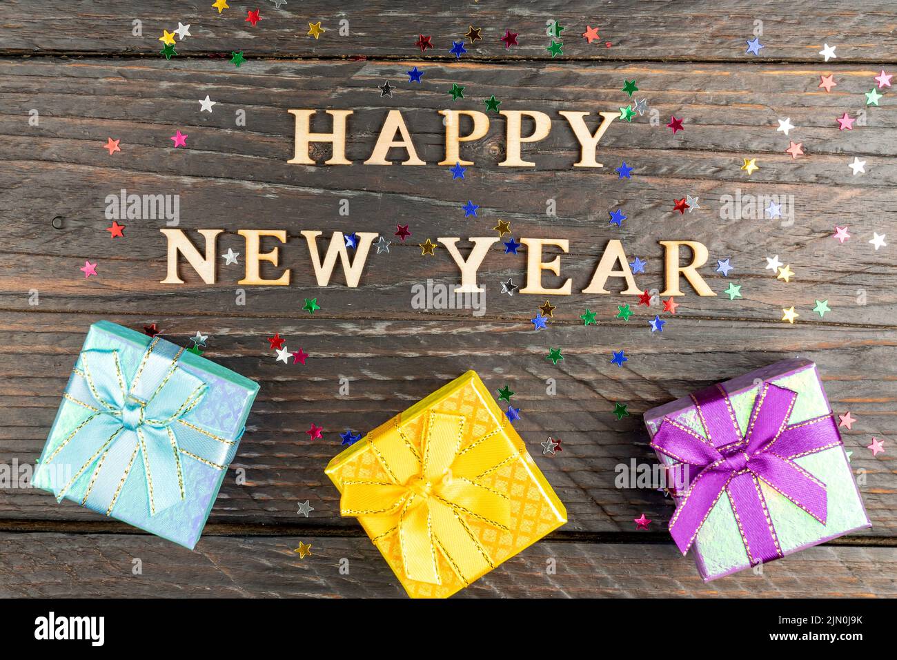 Boîtes-cadeaux multicolores avec noeuds noués. Nouvel an présente sur une table en bois avec des étoiles confetti éparpillées. Texte Bonne Année. Carte de vœux de fête. F Banque D'Images