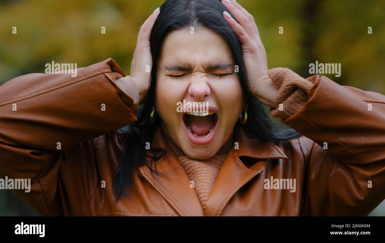 Portrait agacé jeune femme hispanique à l'extérieur criant bruyamment dans la rage ouverture mally bouche tenant les mains sur la tête maux de tête sensation de douleur frustrée Banque D'Images