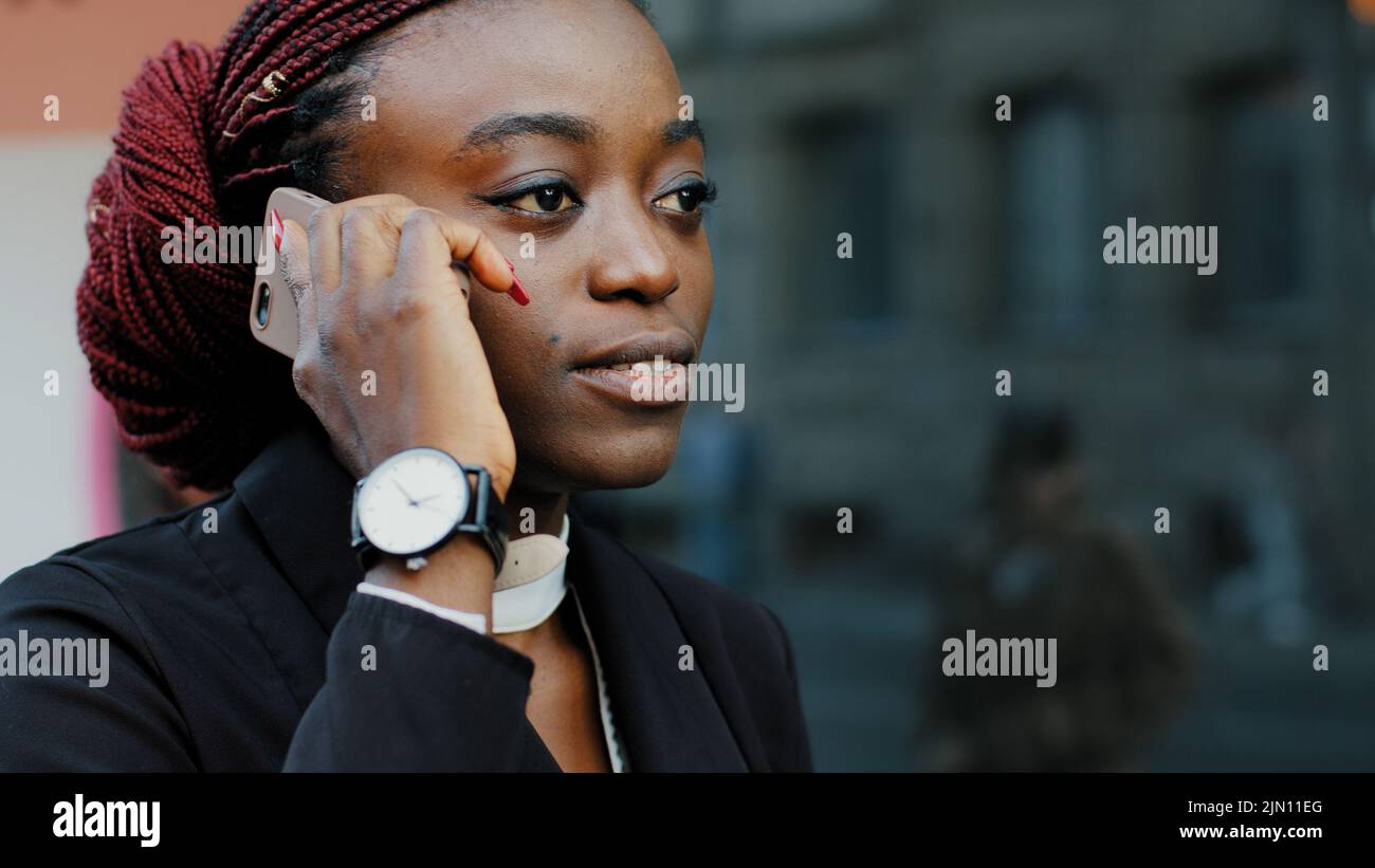 Joyeuse jeune femme d'affaires afro-américaine en plein air bavardant volontiers sur téléphone cellulaire avec ses collègues amis. Fille étudiante souriante femme Banque D'Images