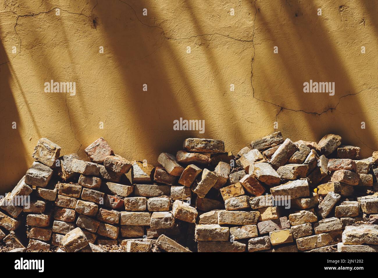 Pile de vieilles briques empilées dans la cour arrière de la maison, penchée sur le mur jaune, espace de copie inclus Banque D'Images