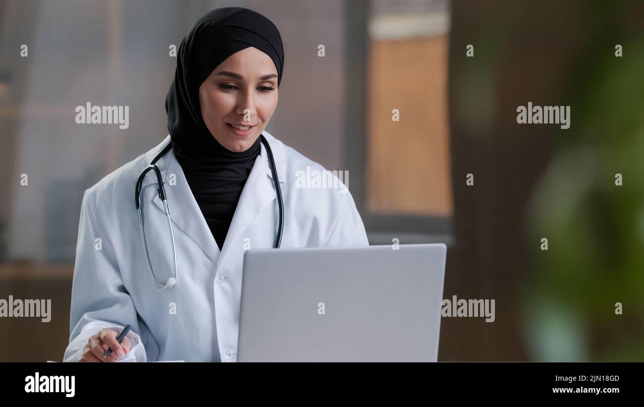 Femme arabe thérapeute médecin porter hijab manteau blanc appelant patient distant sur ordinateur portable parler avec le client dans la télé-télésanté télétéléphonique chat vidéo Banque D'Images