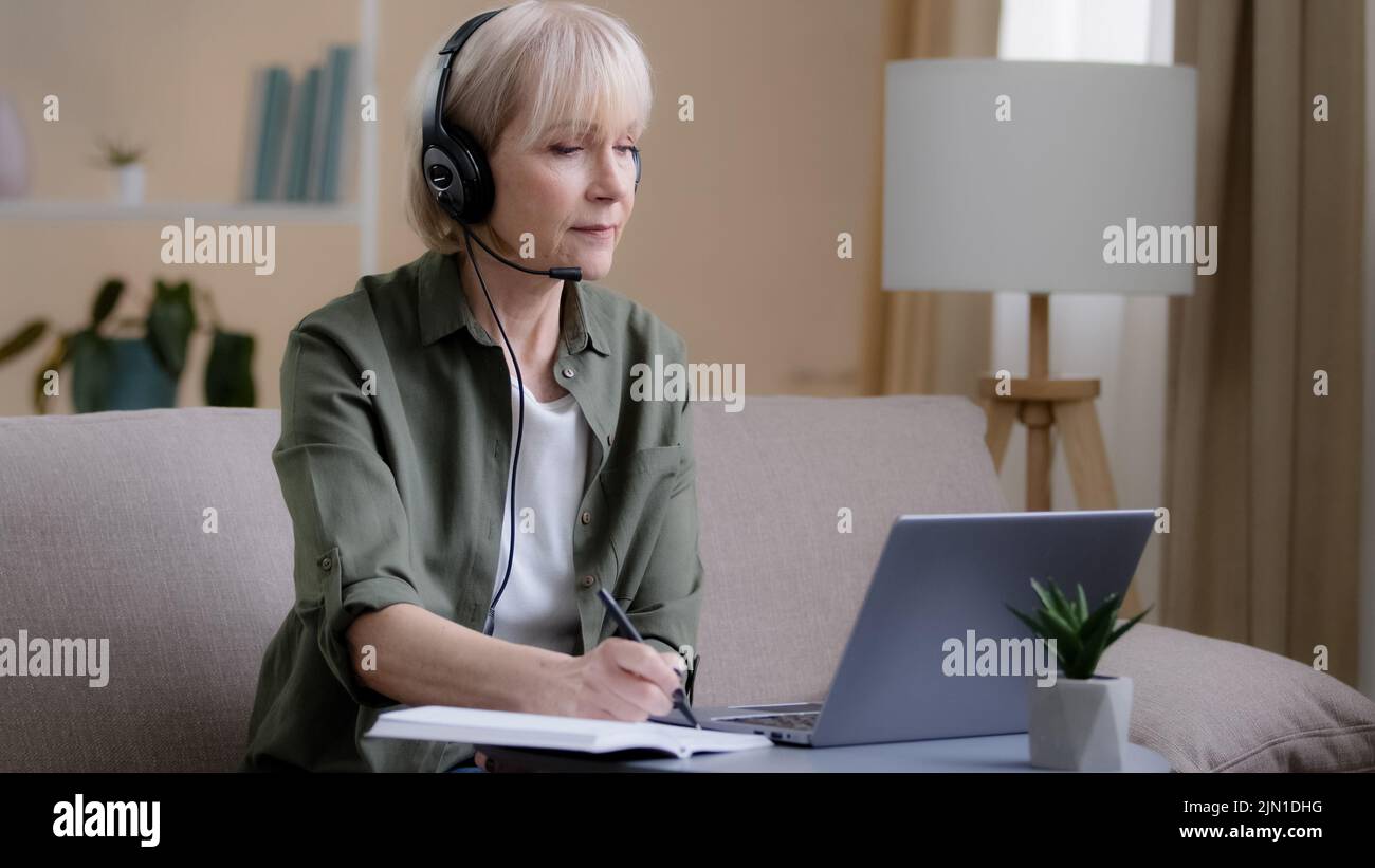 Femme d'affaires senior dans un casque assis sur un canapé Écoutez la formation en ligne webinar e-learning distant 60s femme classe affaires chat vidéo appel Banque D'Images