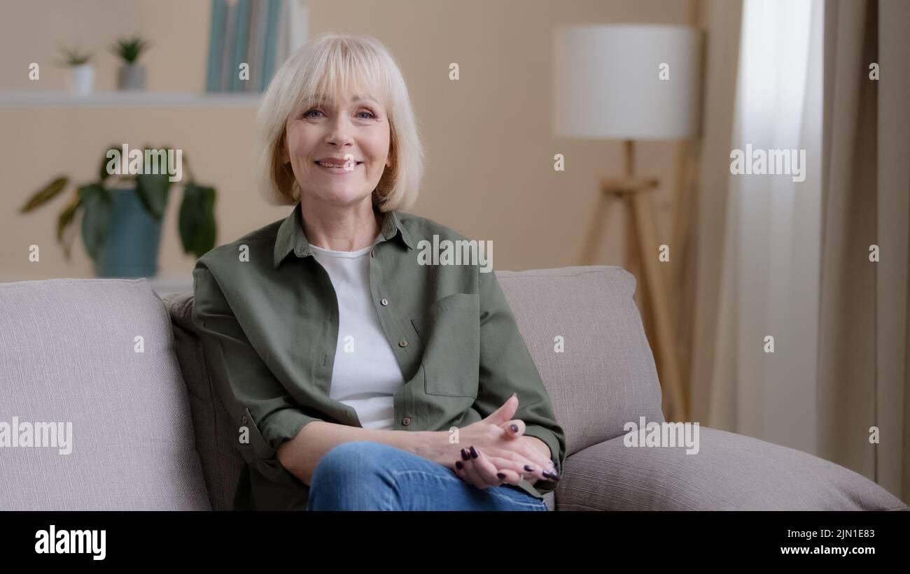 Portrait à la maison pensive pensant souriant belle femme de race blanche adulte plus âgée regardant loin la fenêtre rêvant se tourner vers l'appareil photo assis sur le canapé senior Banque D'Images