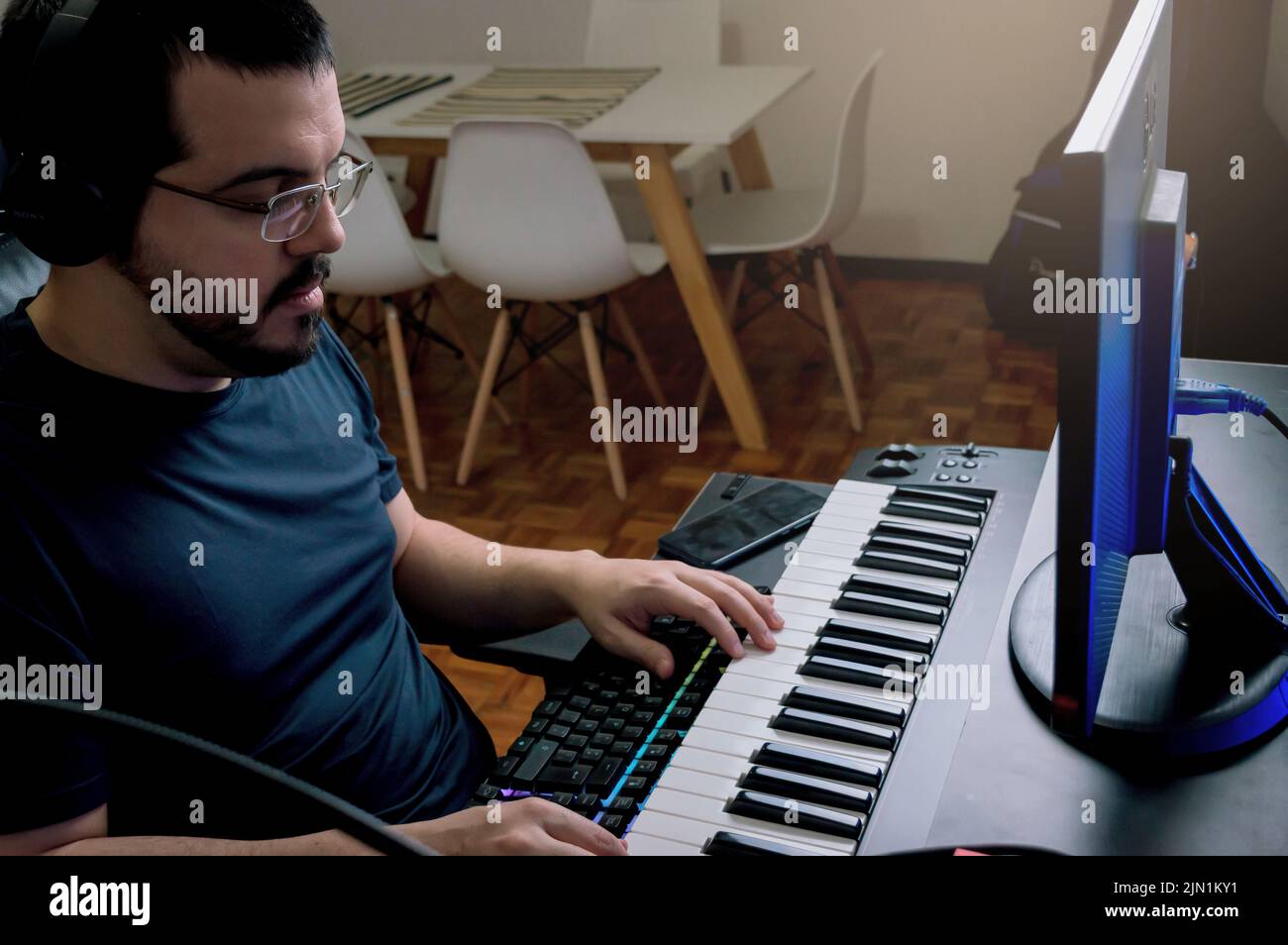 Latino caucasien vénézuélien jeune homme avec la barbe et des lunettes à la maison étudiant des leçons de piano électrique en ligne, jouant du piano regardant le clavier. Banque D'Images