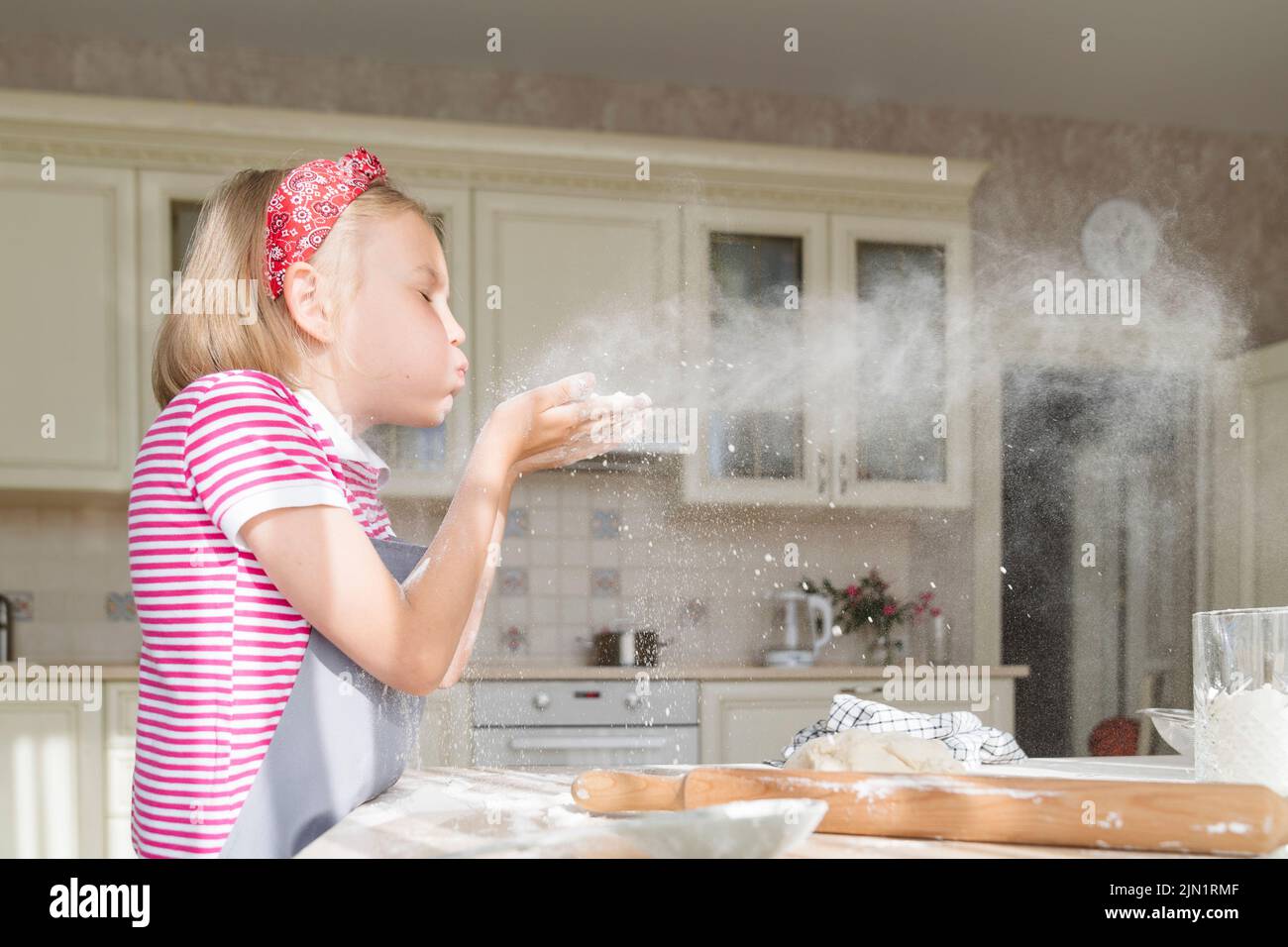 La fille souffle sur la farine dans la cuisine. Banque D'Images