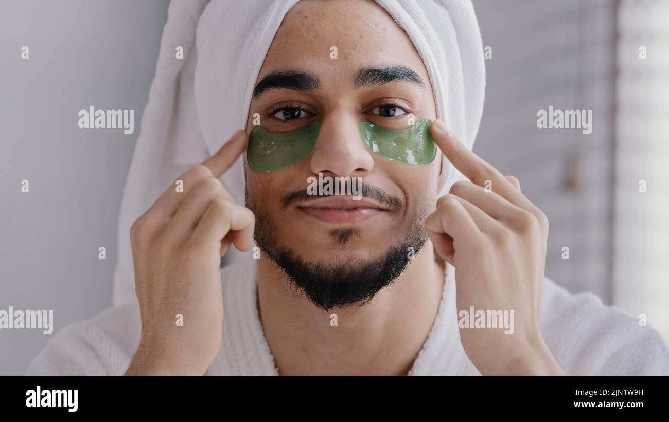 Vue de face portrait homme visage souriant indien arabe homme portant une serviette de bain tête colle hydrogel collants yeux-patchs cosmétiques soins de la peau gars Banque D'Images