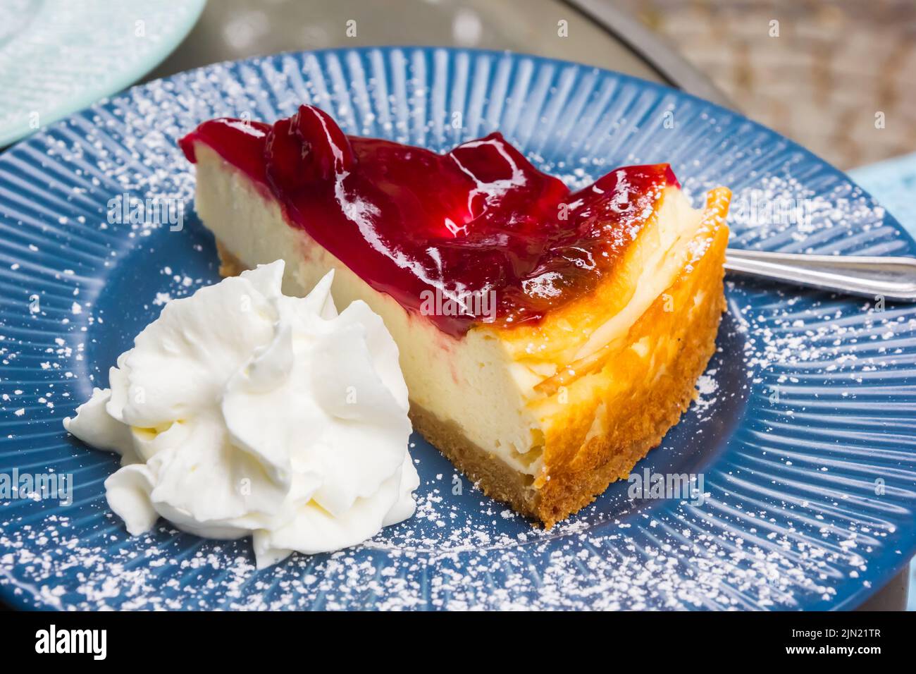 Morceau de gâteau aux fraises avec crème fouettée et sucre en poudre sur une assiette bleue Banque D'Images