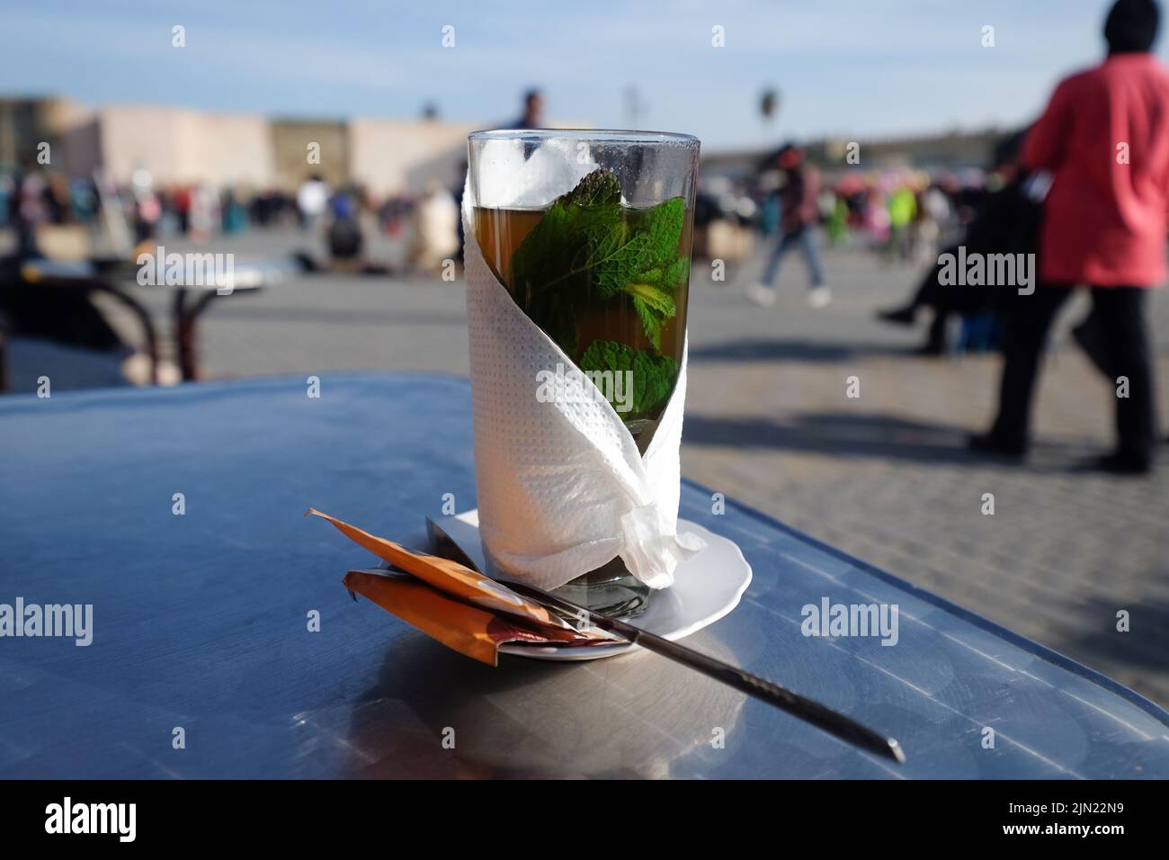 Thé traditionnel à la menthe marocaine chaud avec feuilles de menthe dans un verre enveloppé de papier de soie sur une table. Marrakech, Maroc. Banque D'Images