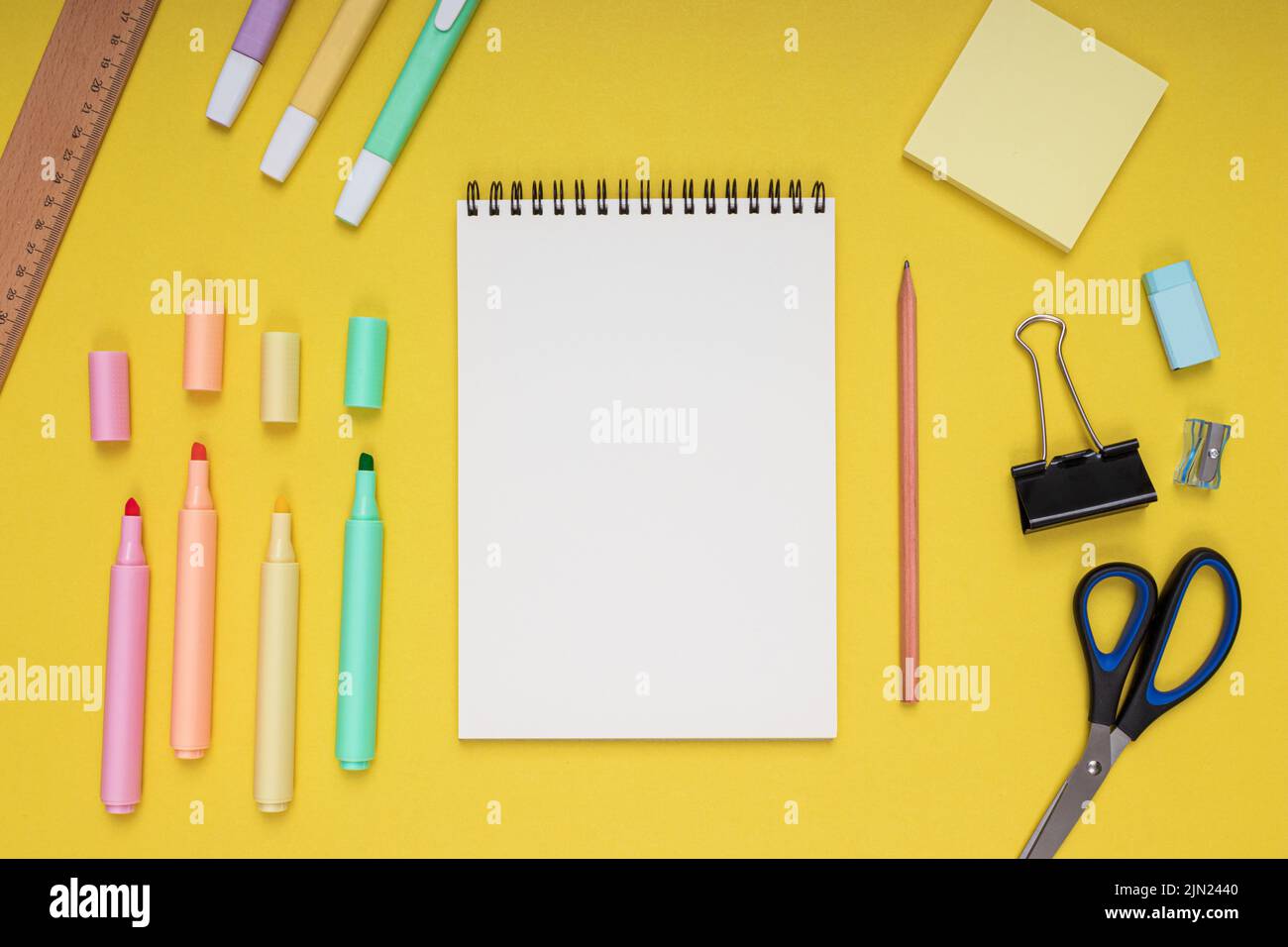 bloc-notes, ciseaux, crayon, taille-crayon, règle, gomme, crayons de couleur, clips et papier à notes. retour à l'école. Arrière-plan jaune isolé Banque D'Images