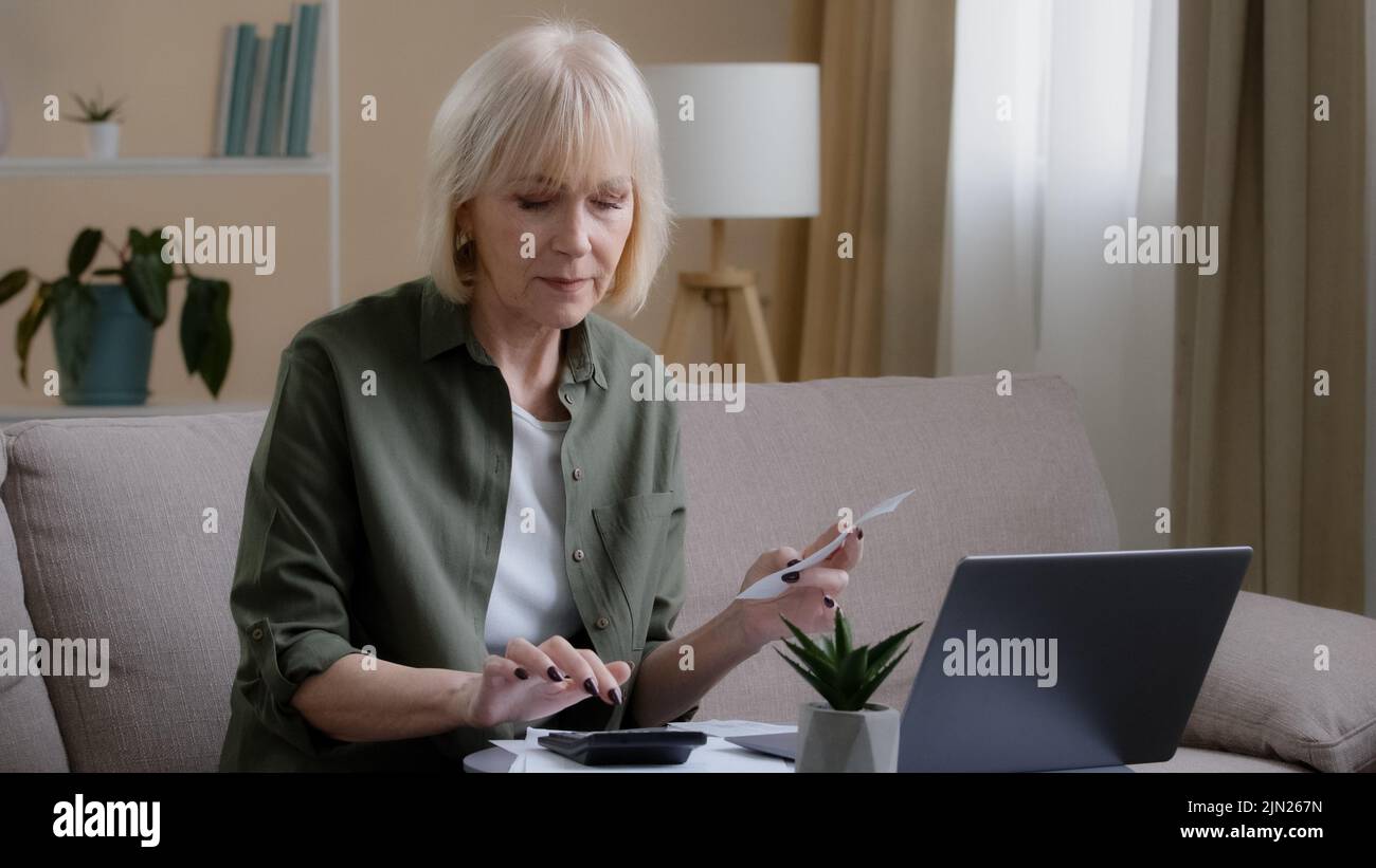 La femme au foyer, vieille femme triste de race blanche, fait des contrôles de budget mensuels sur les revenus en vérifiant les chèques papier à l'aide d'un ordinateur portable d'application. Femme d'affaires d'âge moyen Banque D'Images