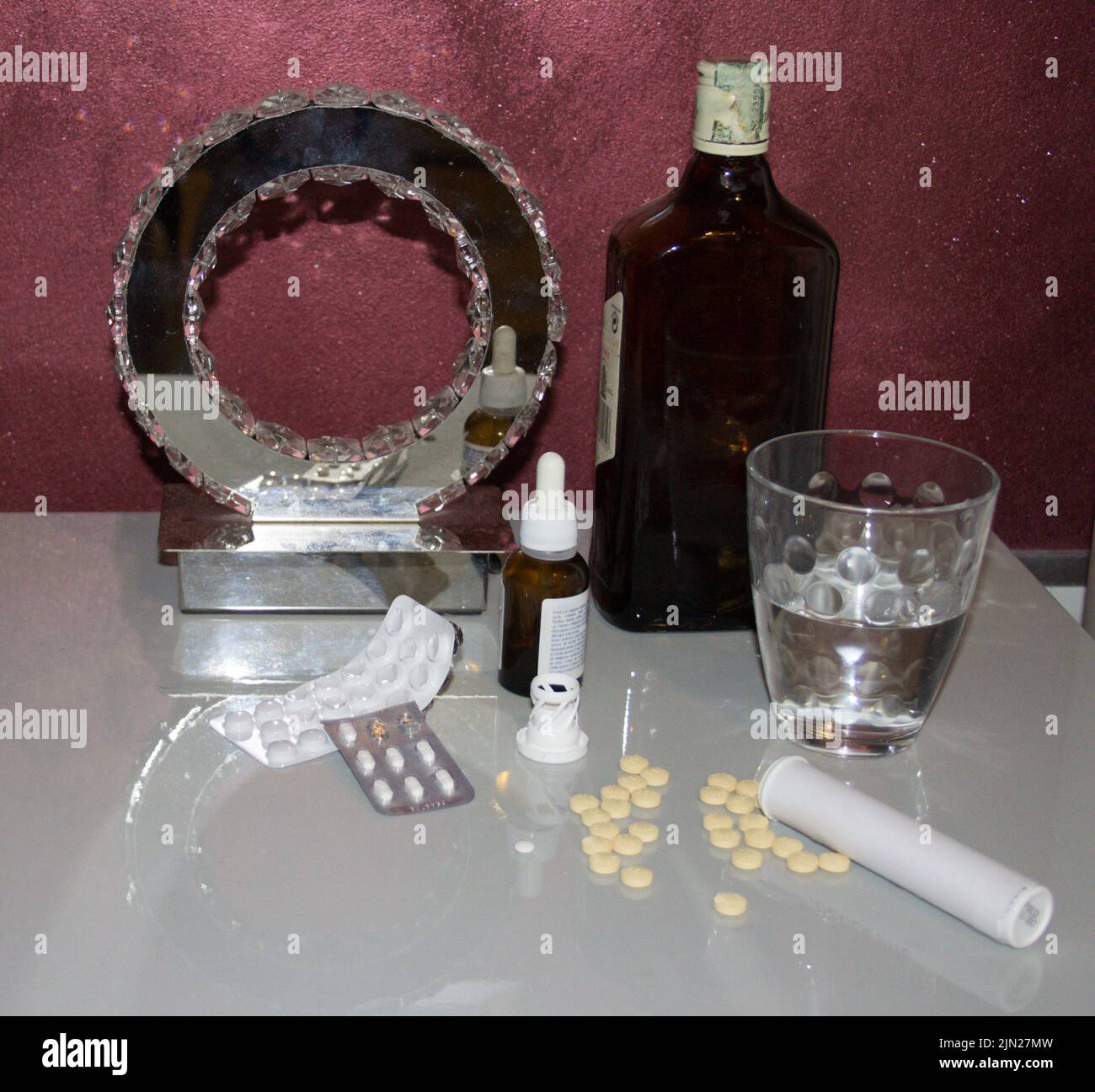 Image d'une table de chevet avec divers médicaments tels que des anxiolytiques et des antidépresseurs, un verre d'eau et une bouteille de whisky. Banque D'Images