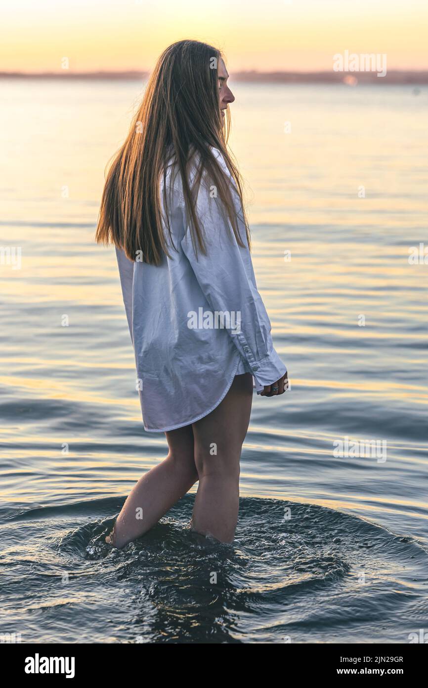 Une femme en maillot de bain et une chemise blanche dans la mer au coucher  du soleil Photo Stock - Alamy