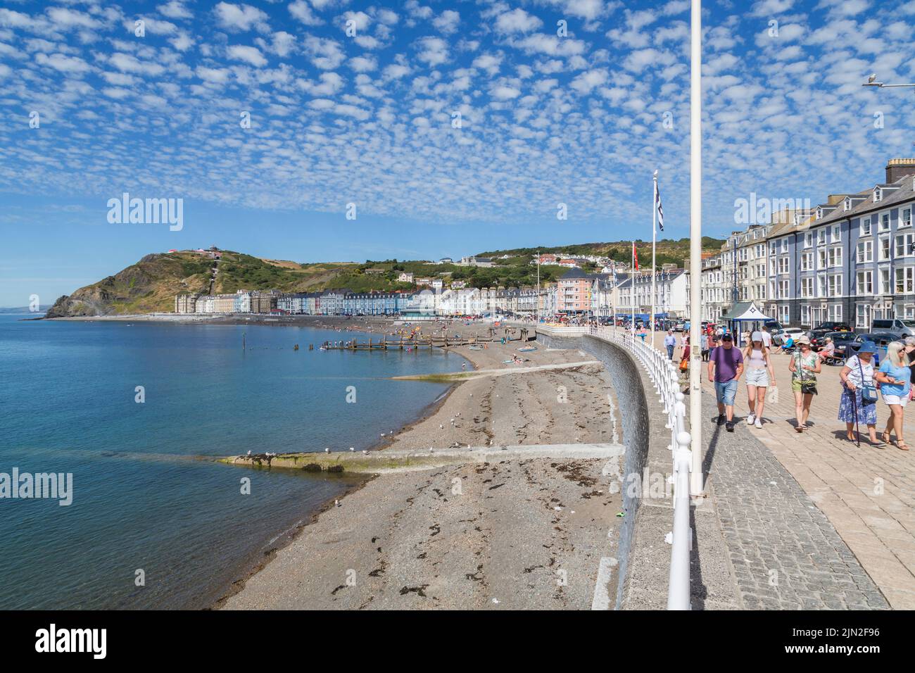 Les touristes se baladent le long de la promenade avec vue sur la mer, la plage et la colline de la Constitution à la station balnéaire gallois d'Aberystwyth. Banque D'Images