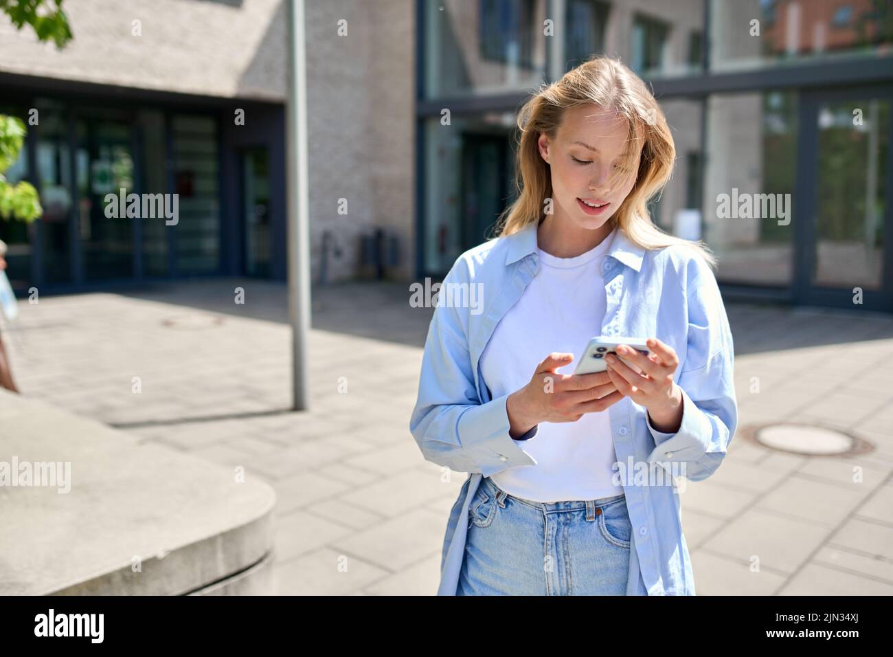 Jeune étudiante universitaire utilisant des applications de smartphone debout à l'extérieur. Banque D'Images