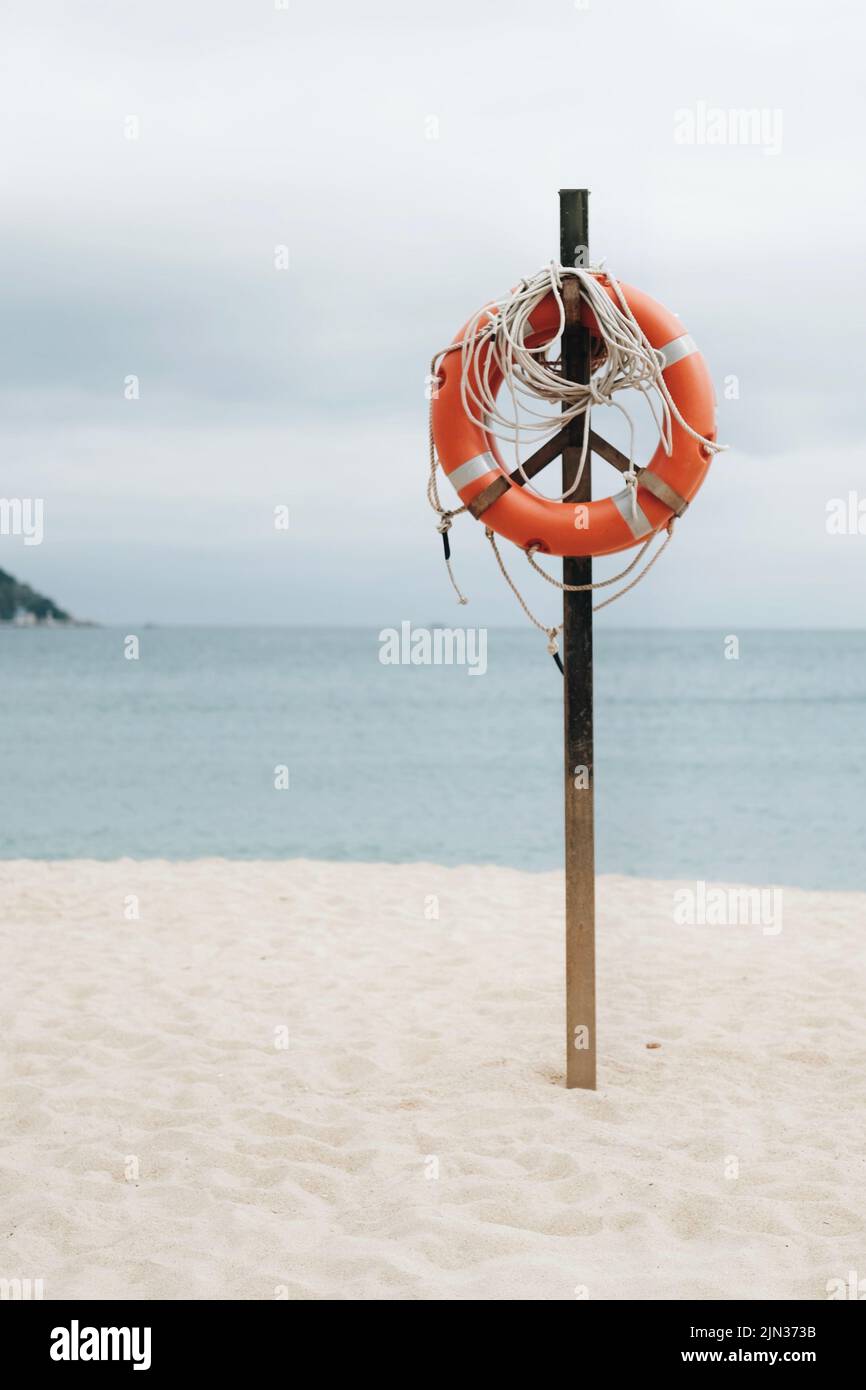 Une photo verticale d'un économiseur d'eau orange accroché à un poteau en bois sur la plage de sable Banque D'Images