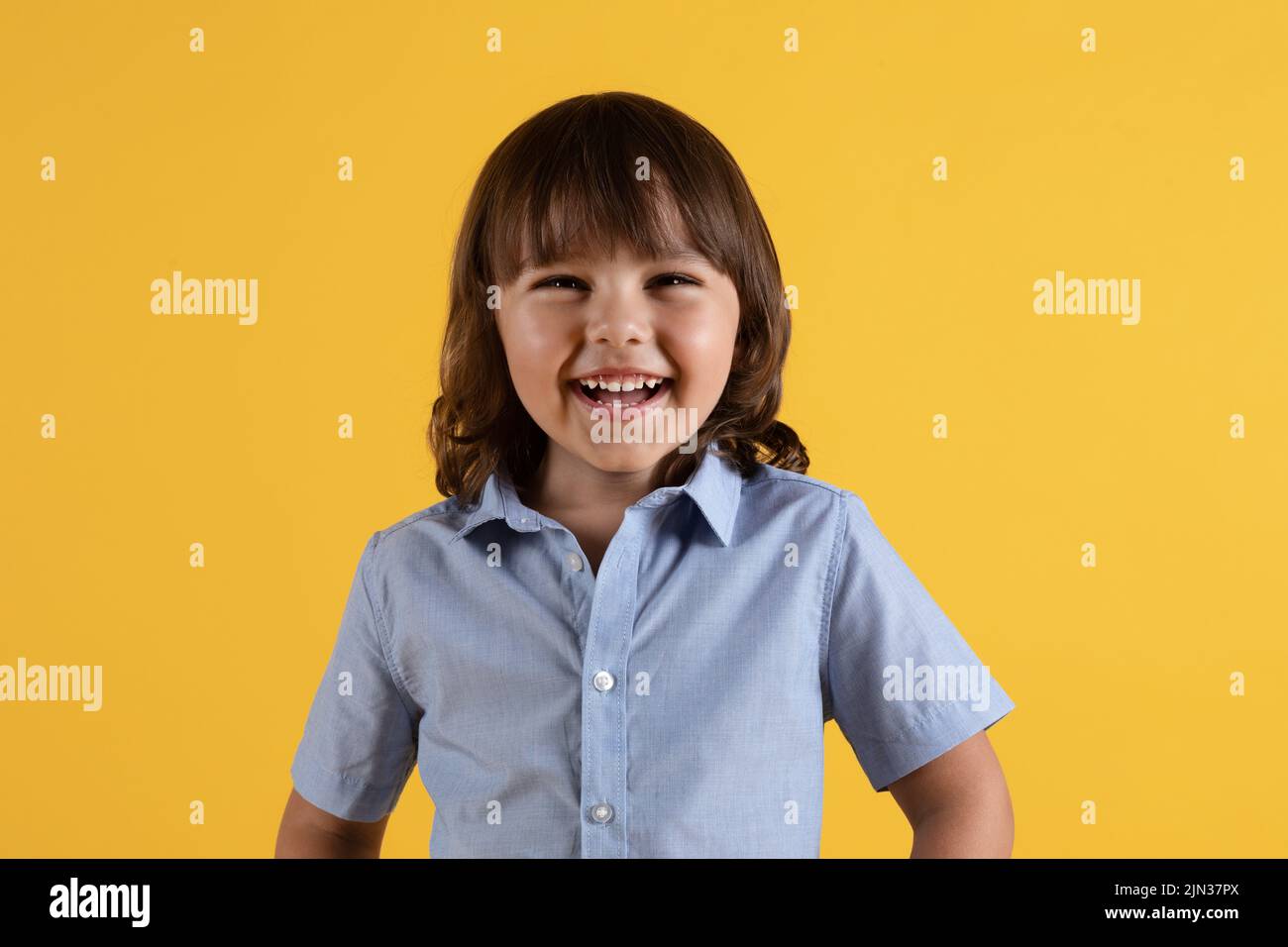 Concept d'enfance heureuse. Adorable garçon positif riant gaiement, regardant l'appareil photo, fond jaune de studio Banque D'Images