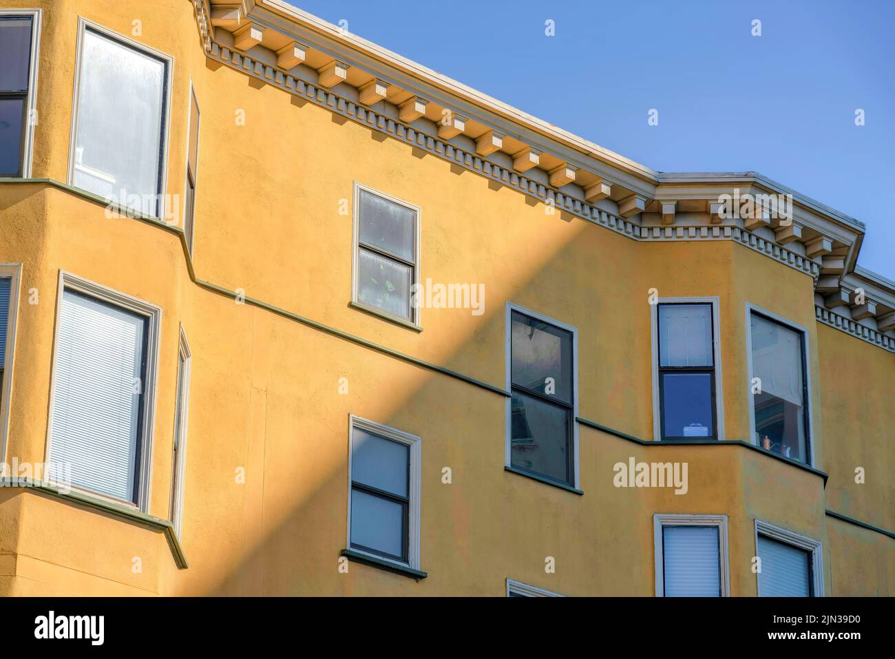 Vue sur un bâtiment résidentiel avec mur en stuc jaune et avant-toits décoratifs à San Francisco, CA. Extérieur du bâtiment d'appartement avec photo et simple Banque D'Images