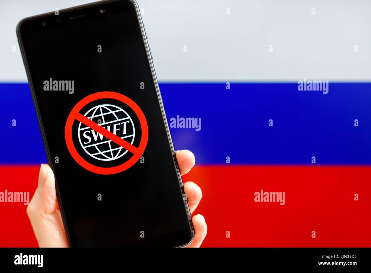 Ukraine, Kiev - février, 23 2022: Main tenant mobile avec le logo SWIFT barré et le drapeau russe en arrière-plan. Sanctions contre la Russie, déconnexion du concept SWIFT. Banque D'Images