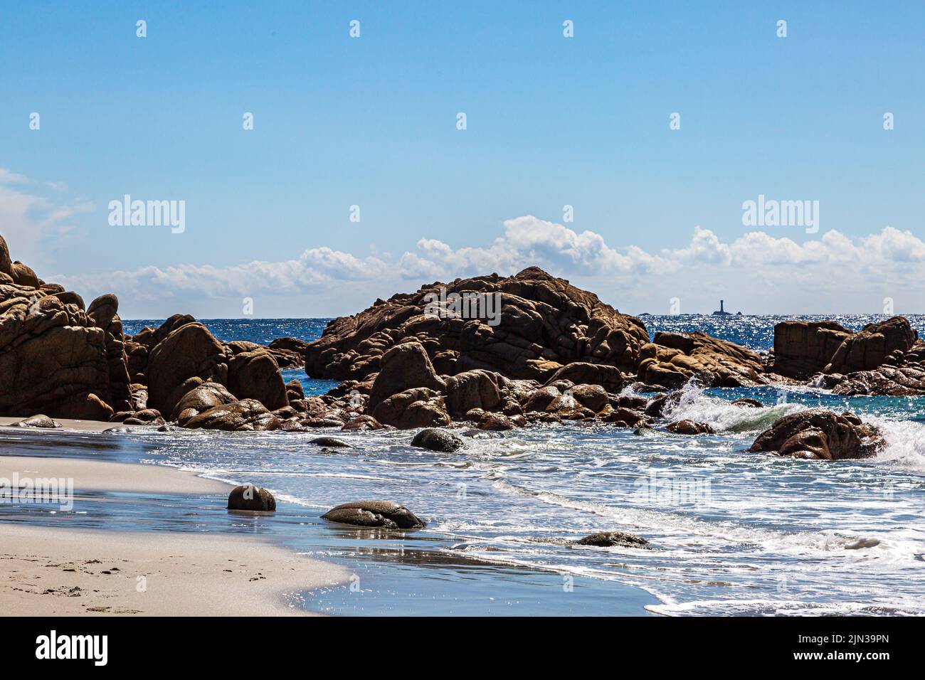 Vue sur la côte rocheuse depuis la plage de Porth Nanven dans les Cornouailles, avec une vue lointaine sur le phare de Longships au large de Land's End Banque D'Images