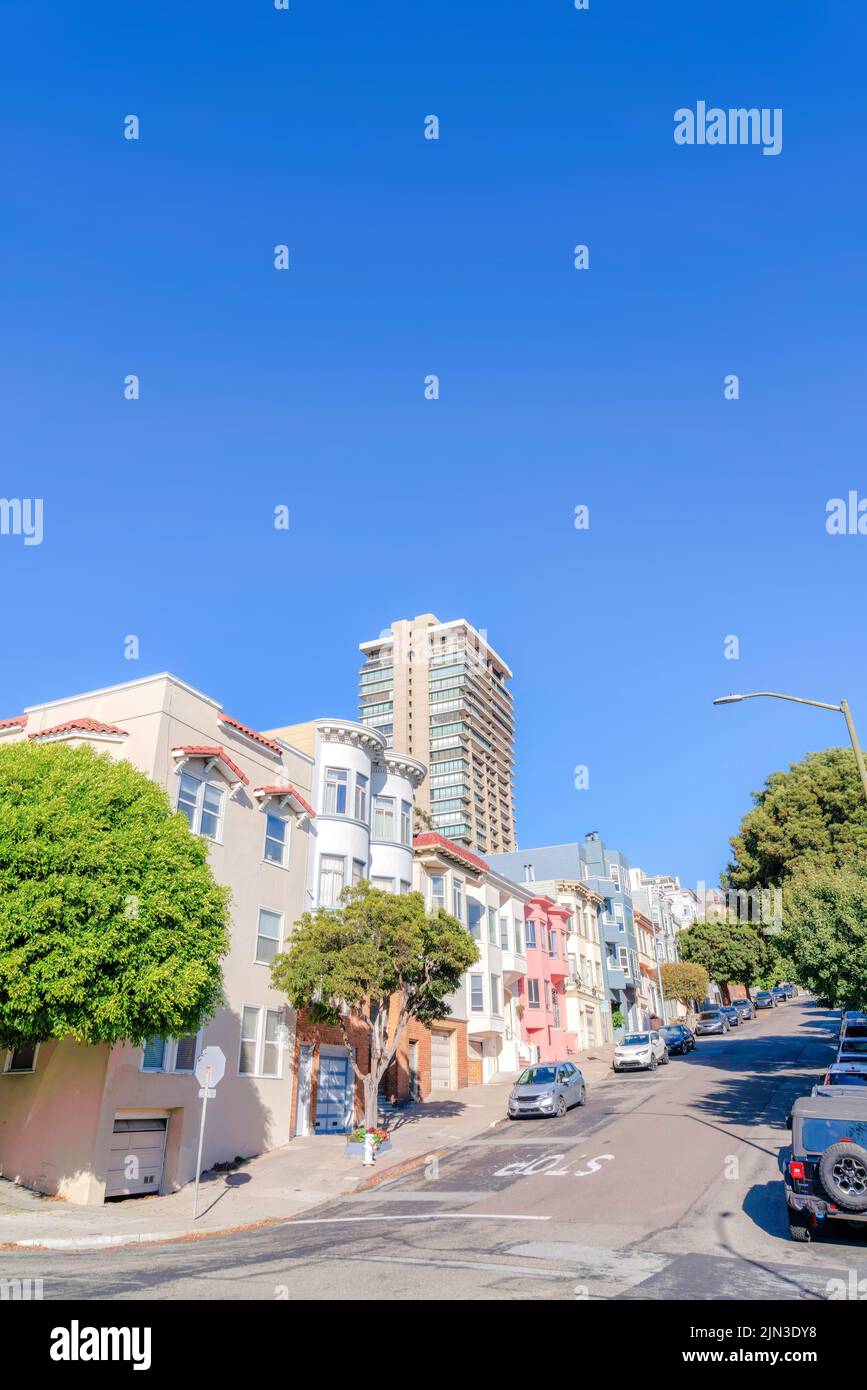 Quartier incliné à San Francisco, CA avec des véhicules et des arbres à l'avant des maisons de ville. Il y a une rangée de maisons de ville avec l'extérieur victorien et Banque D'Images