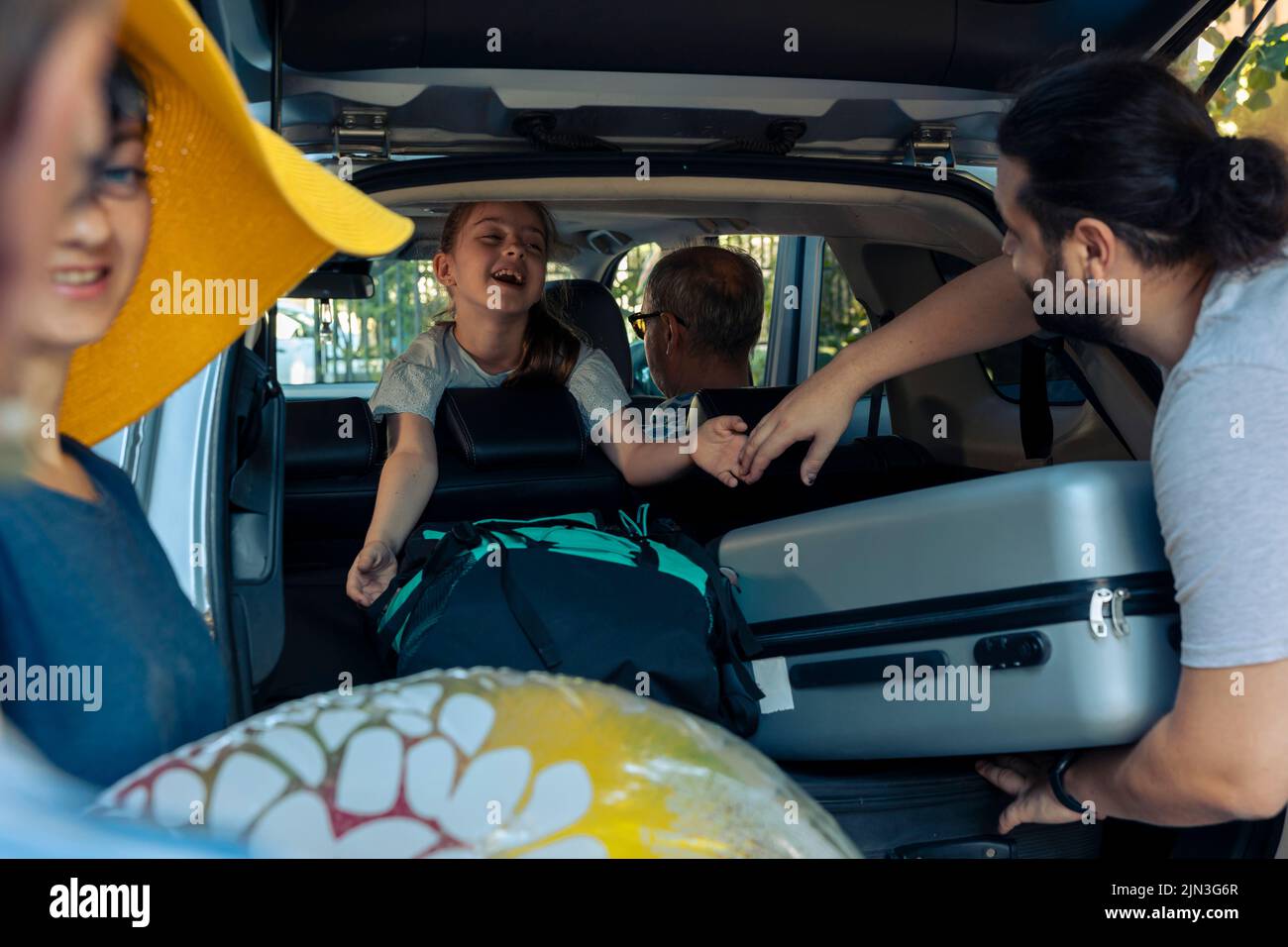 Famille caucasienne voyageant en vacances en voiture, mettant le chariot et les sacs dans le coffre du véhicule. Les parents et grands-parents partent en vacances avec une petite fille, une valise à bagages et des bagages. Banque D'Images