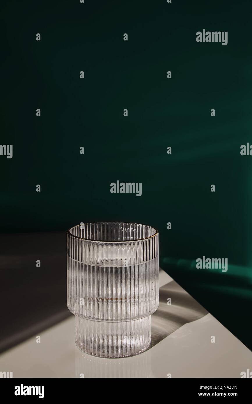 Verre d'eau propre à la mode et à la lumière du soleil sur la table blanche au-dessus du mur vert Banque D'Images