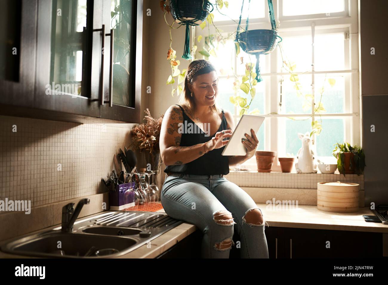 Femme édomque, curvy et détendue sur une application de médias sociaux en ligne ou regardant du contenu Internet amusant dans la cuisine. Femme heureuse, insouciante et élégante Banque D'Images