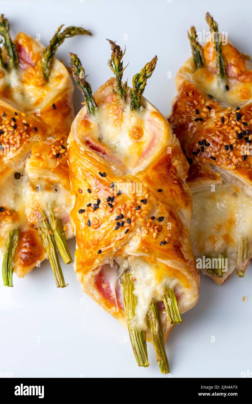 Asperges vertes cuites au jambon et au fromage dans une pâte feuilletée parsemée de graines de sésame et de feuilles de basilic vert. Banque D'Images