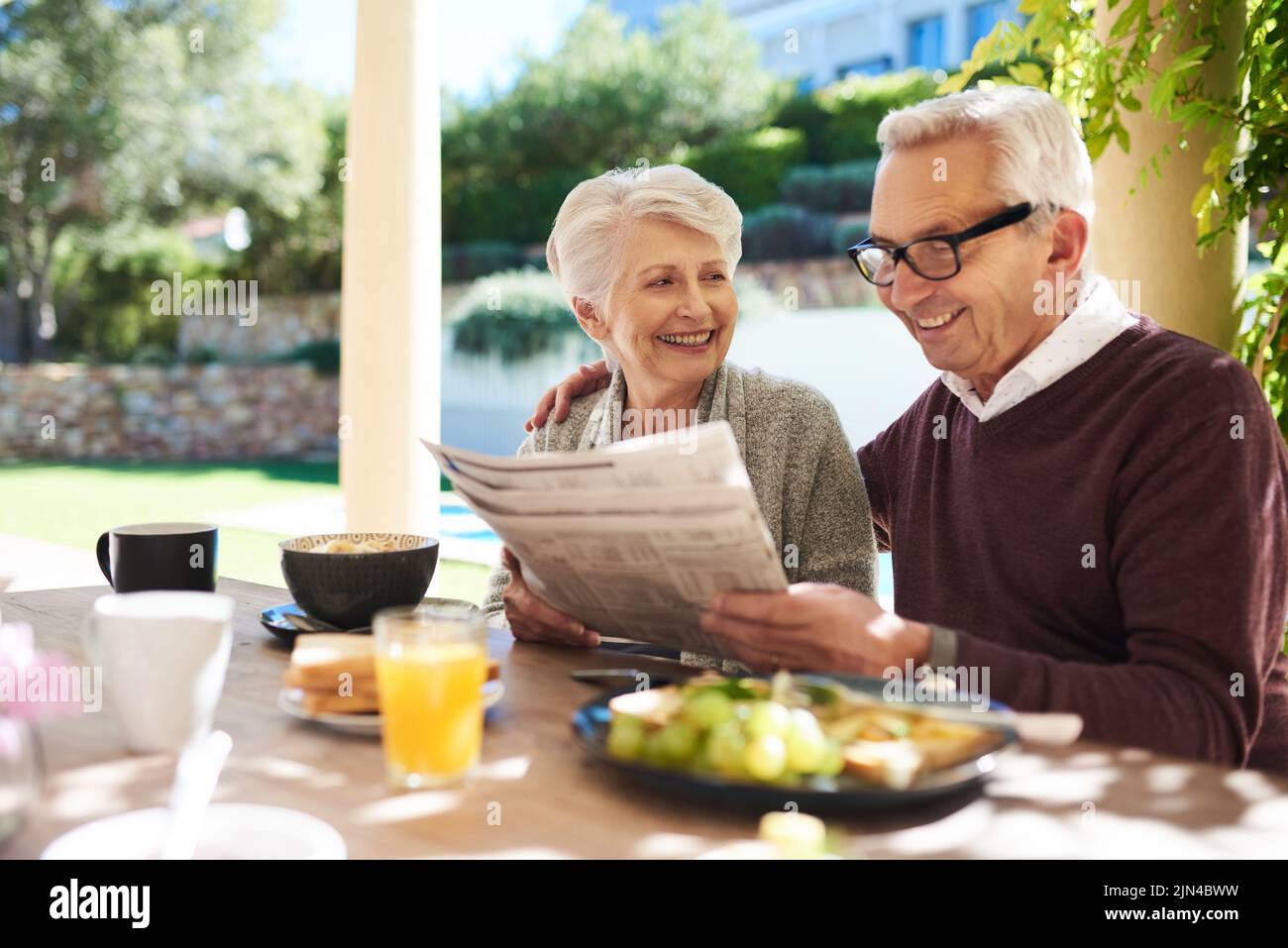 C'est ainsi que nous nous gardons dans la boucle. Un couple affectueux senior lisant le journal tout en appréciant un repas ensemble à l'extérieur. Banque D'Images