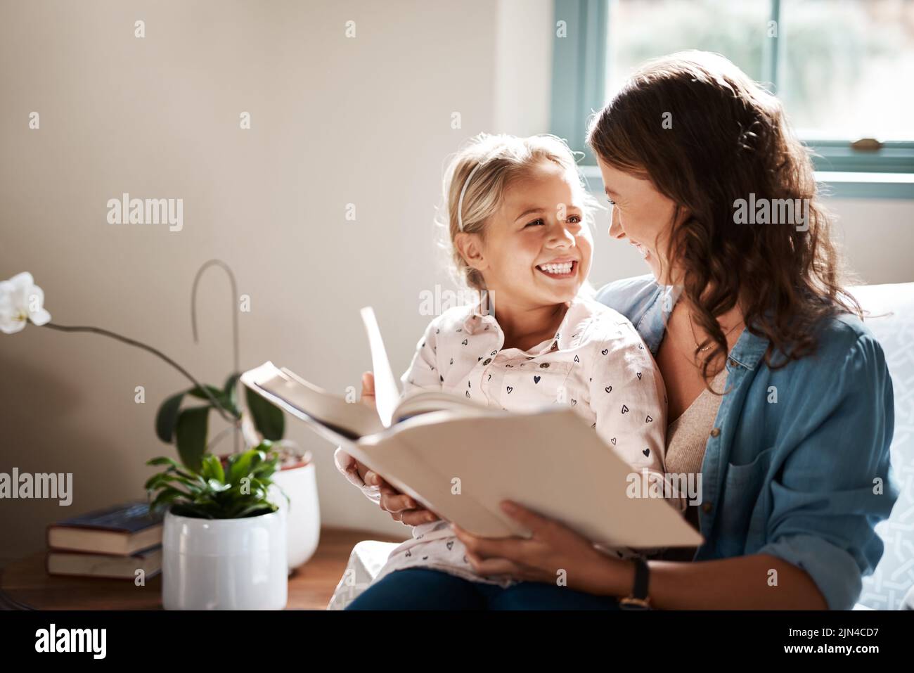 Maman fait l'apprentissage pour lire amusant. Une adorable petite fille lisant un livre avec sa mère sur le canapé à la maison. Banque D'Images