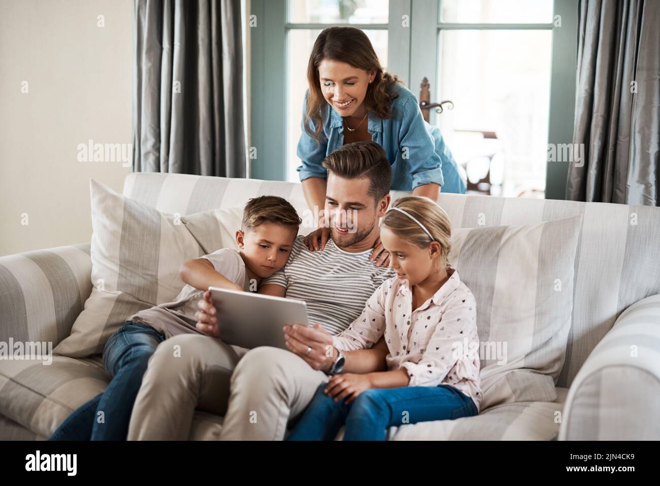 Transformer la technologie en un outil d'apprentissage. Une jeune famille heureuse de quatre personnes utilisant une tablette numérique sur le canapé à la maison. Banque D'Images