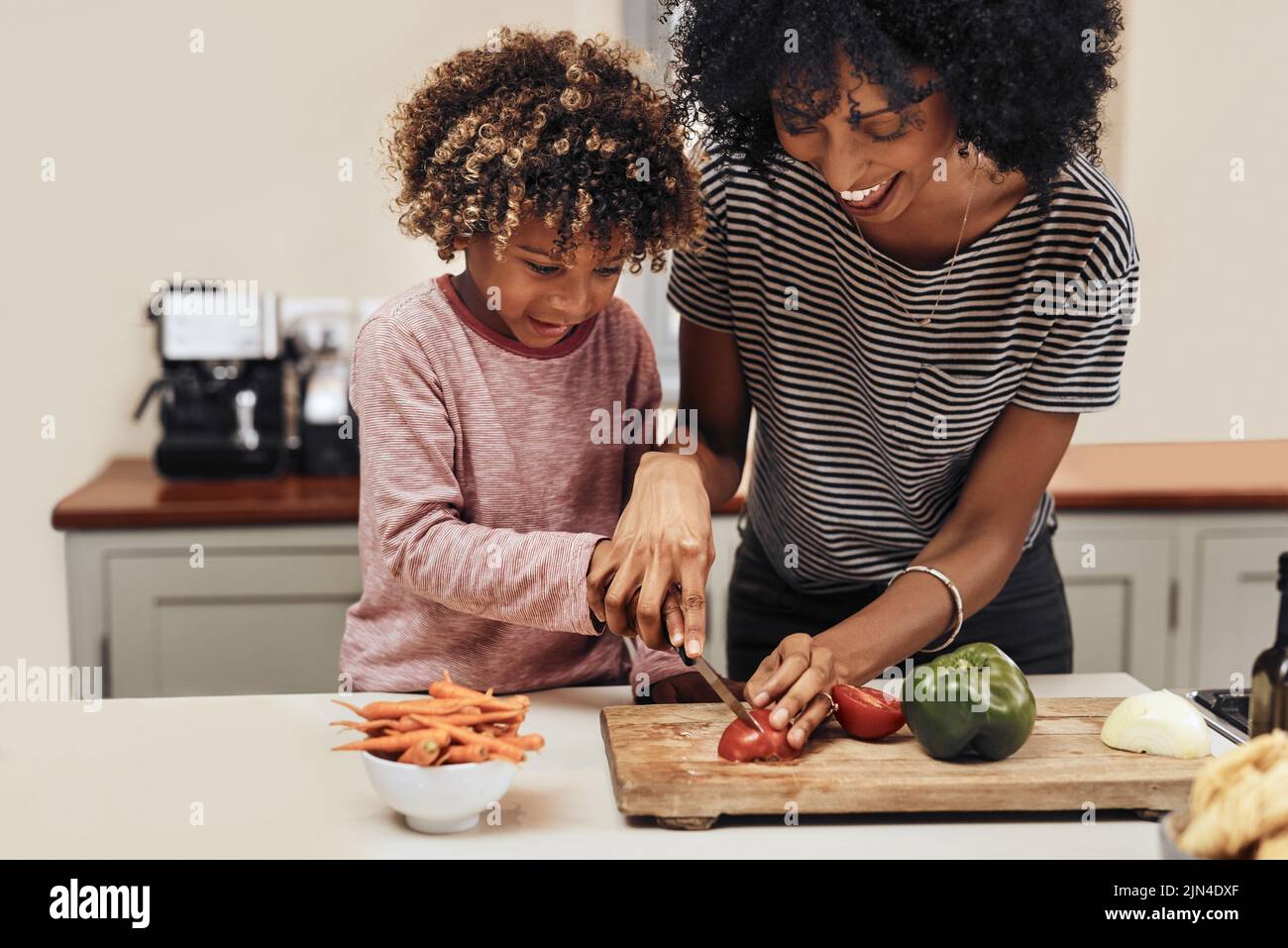 Vous le faites bien. Un jeune garçon coupant des légumes avec l'aide de sa mère. Banque D'Images