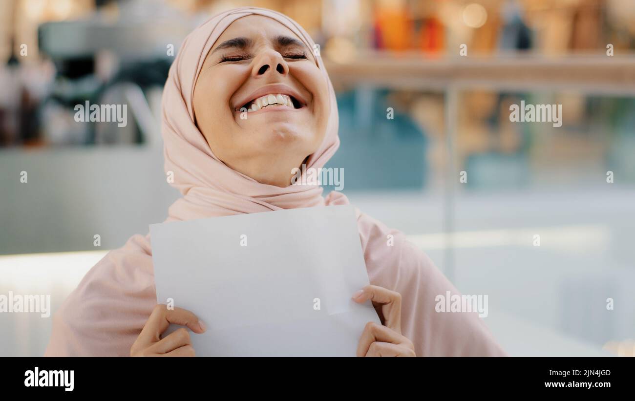 Gros plan jeune femme arabe heureuse et excitée dans le hijab recevant une lettre lisant de bonnes nouvelles incroyables souriant excellent résultat de test médical approuver pour nouveau Banque D'Images