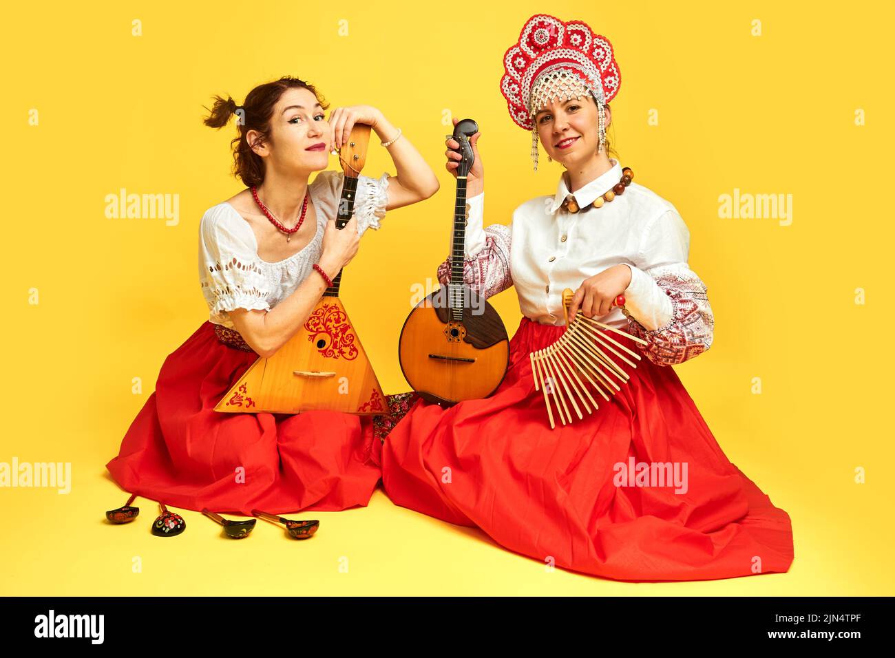 Femmes musiciens dans des robes folkloriques russes avec des instruments de musique sur fond jaune studio. Des artistes heureux de Russie dans des vêtements nationaux avec str Banque D'Images