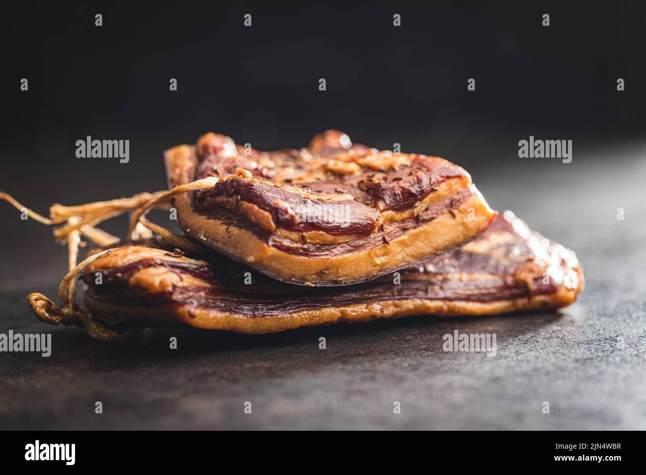 Bacon fumé entier sur une table noire. Banque D'Images