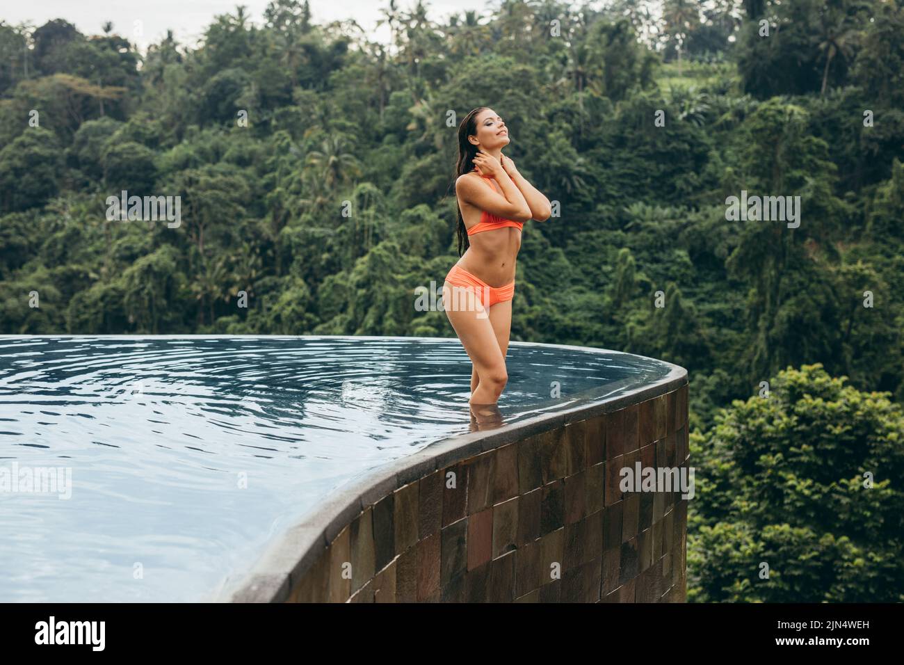 Photo d'une jeune femme portant un bikini orange debout dans la piscine, à la station de vacances. Profiter de ses vacances à la piscine. Banque D'Images