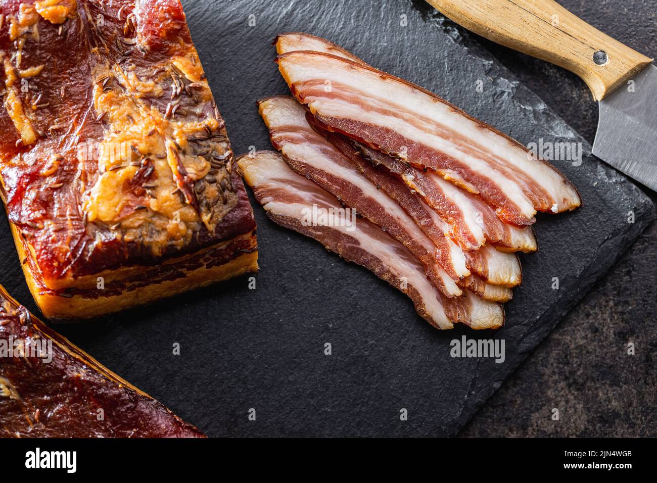 Bacon fumé entier et en tranches sur une table noire. Vue de dessus. Banque D'Images