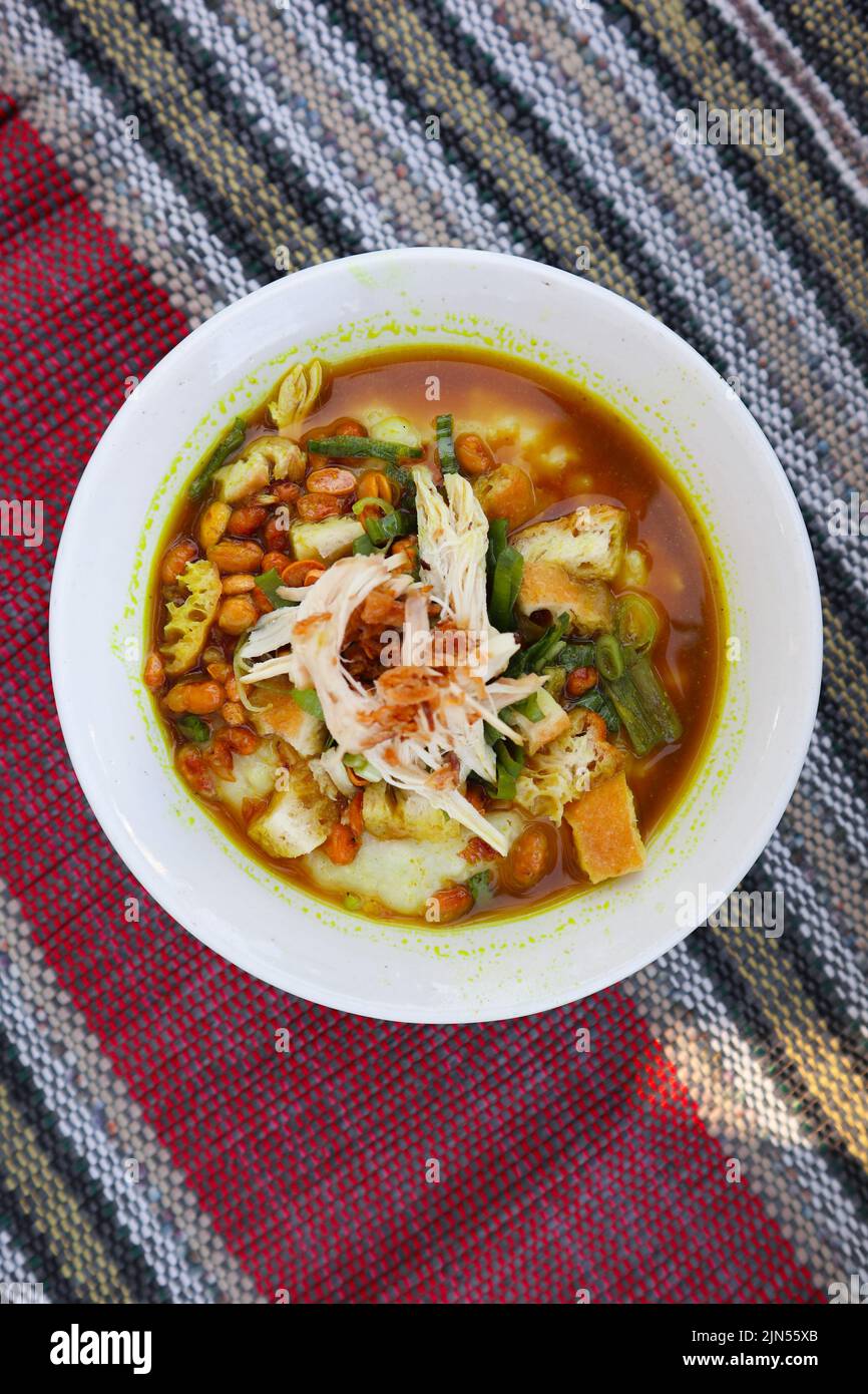 bur ayam ou porridge de poulet ou bouillie de riz, servi avec du poulet râpé, une tranche de poireaux, des haricots et un bol blanc, isolé sur fond noir Banque D'Images